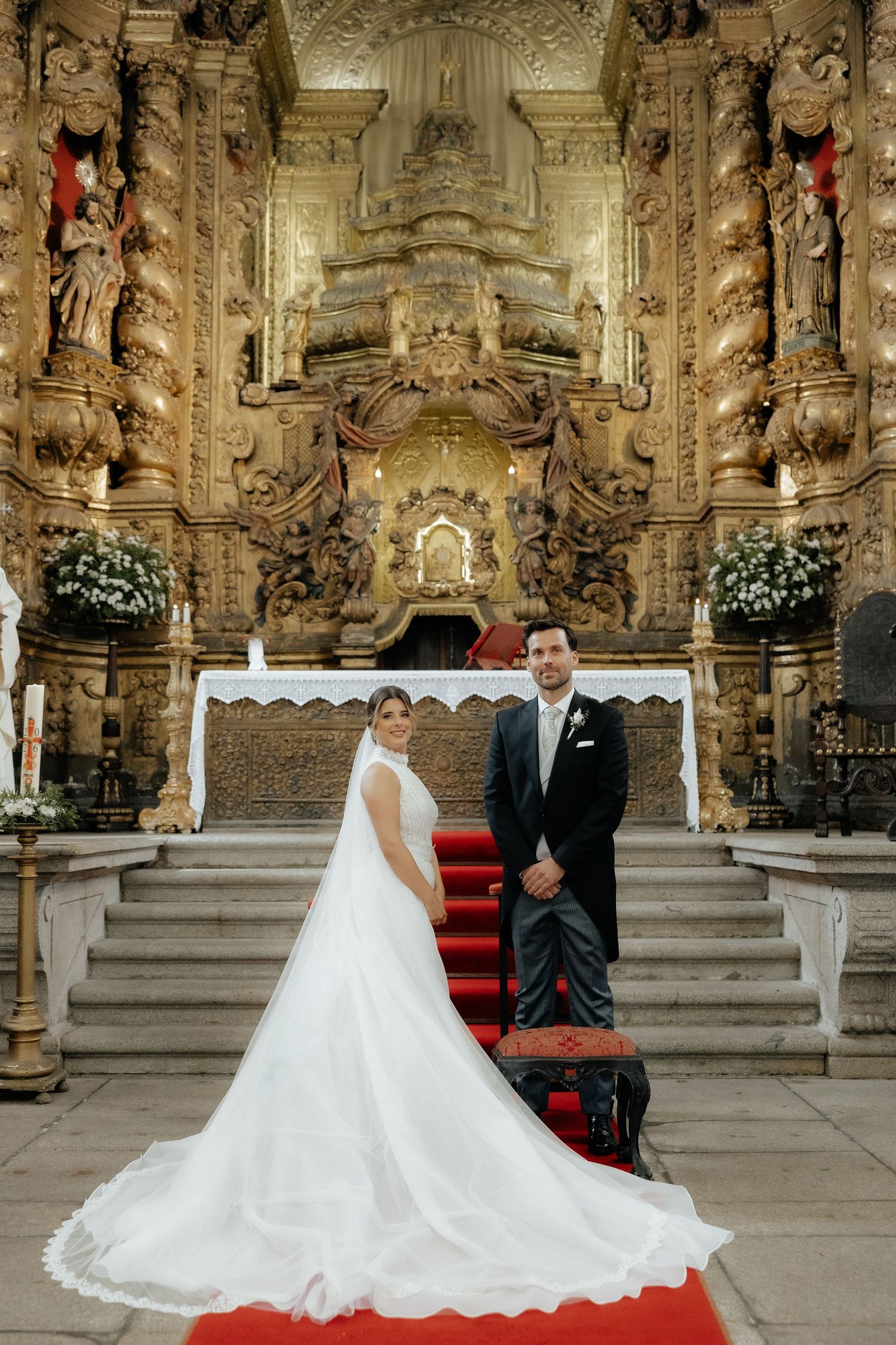 Bride and groom pose before ornate golden baroque church altar on wedding day.