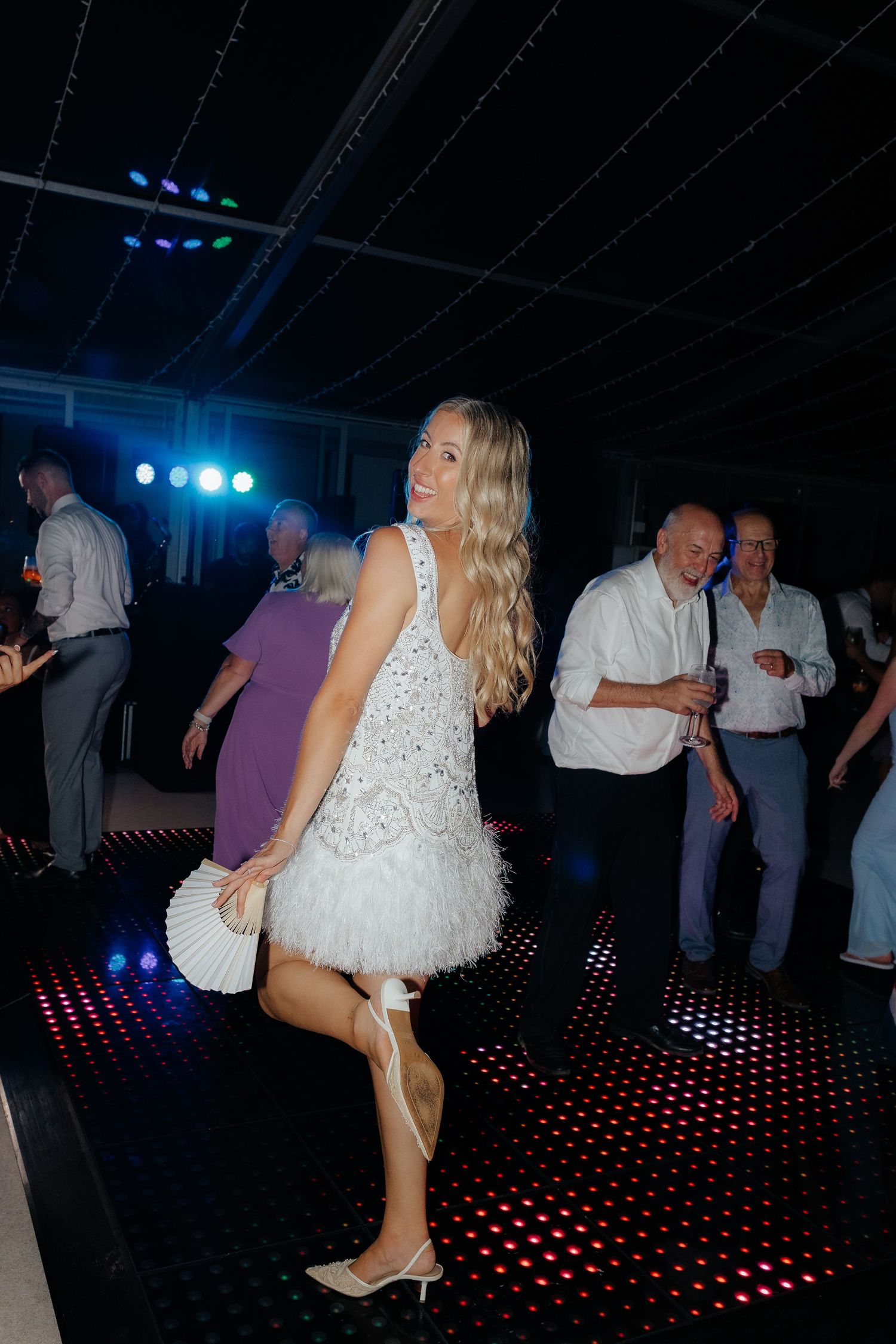 People dancing on an illuminated dance floor with red LED lights and blue stage lighting in a dark venue.
