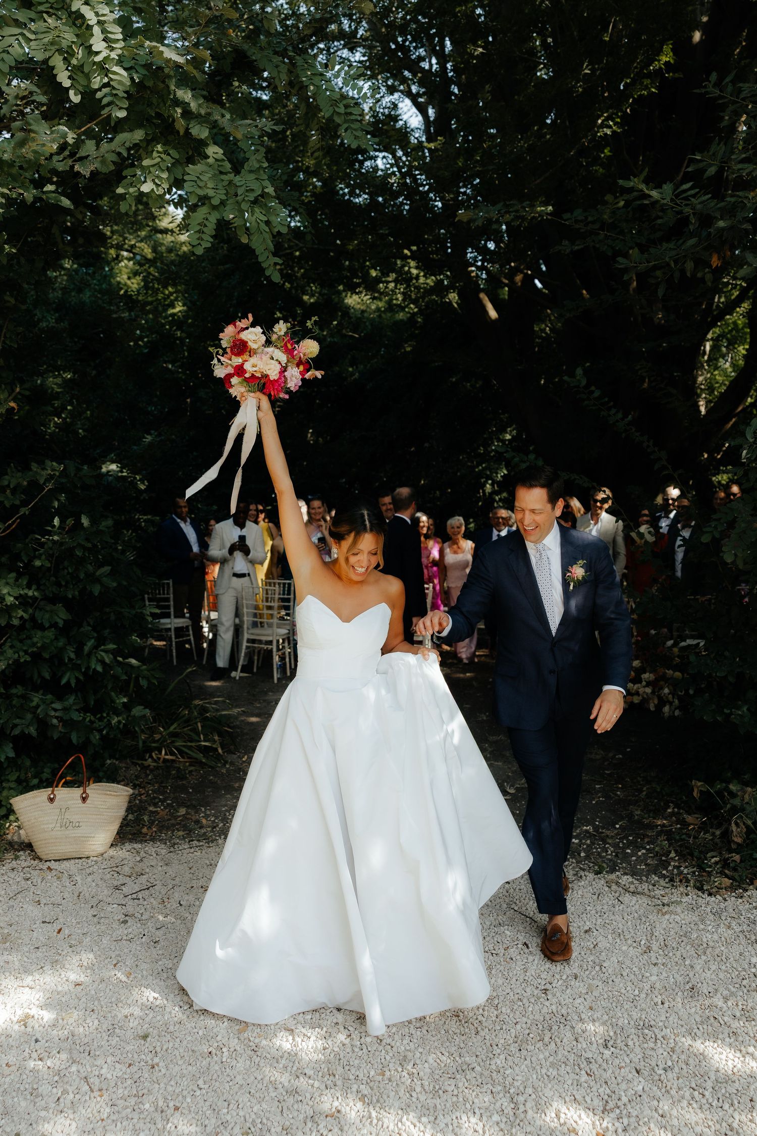 Wedding celebration on gravel path with bride in white gown and colorful bouquet.