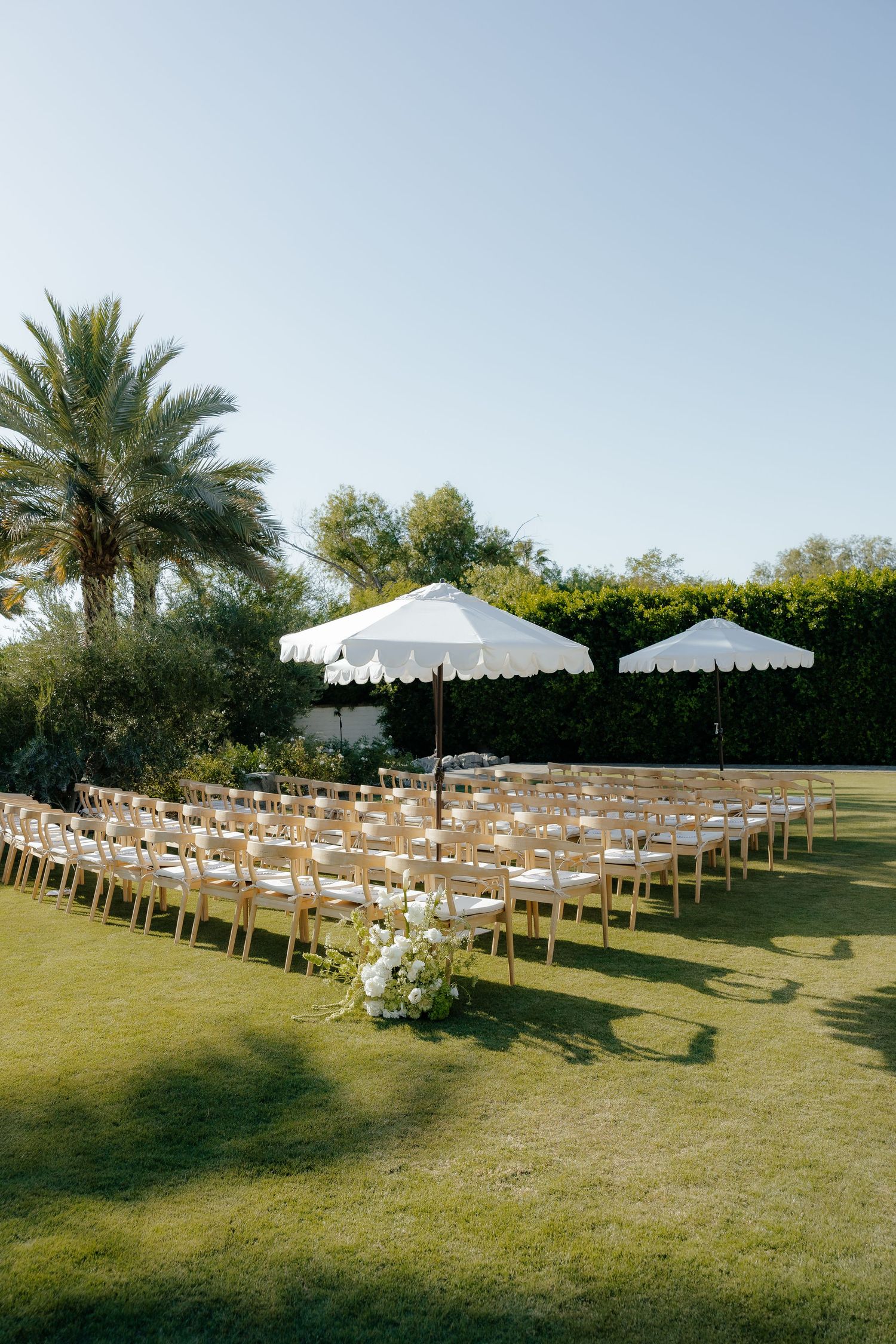 Outdoor wedding ceremony venue with wooden chairs and white scalloped umbrellas on green lawn.