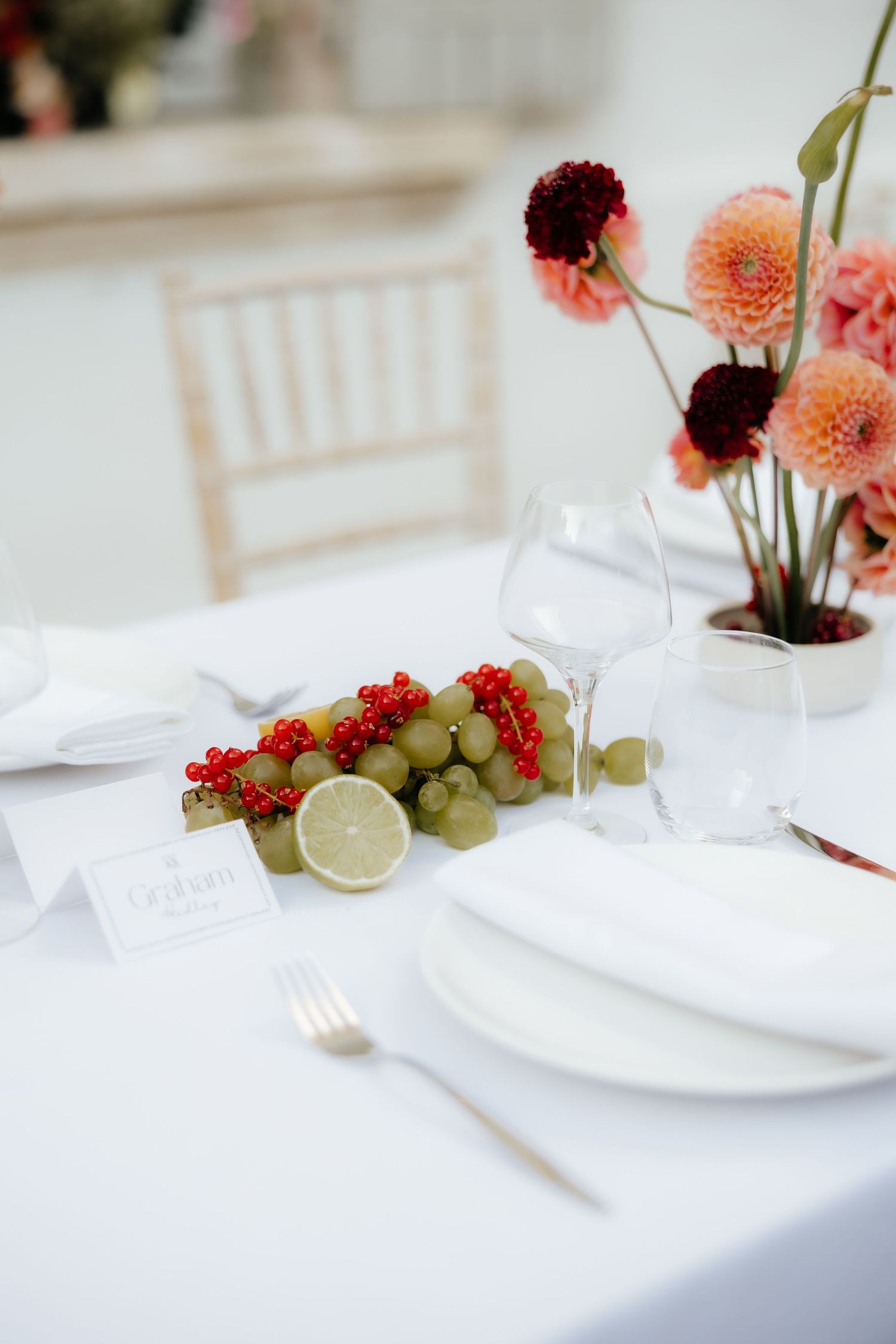 Elegant table setting with pink dahlia flowers, red currants, grapes and lime on crisp white linens.