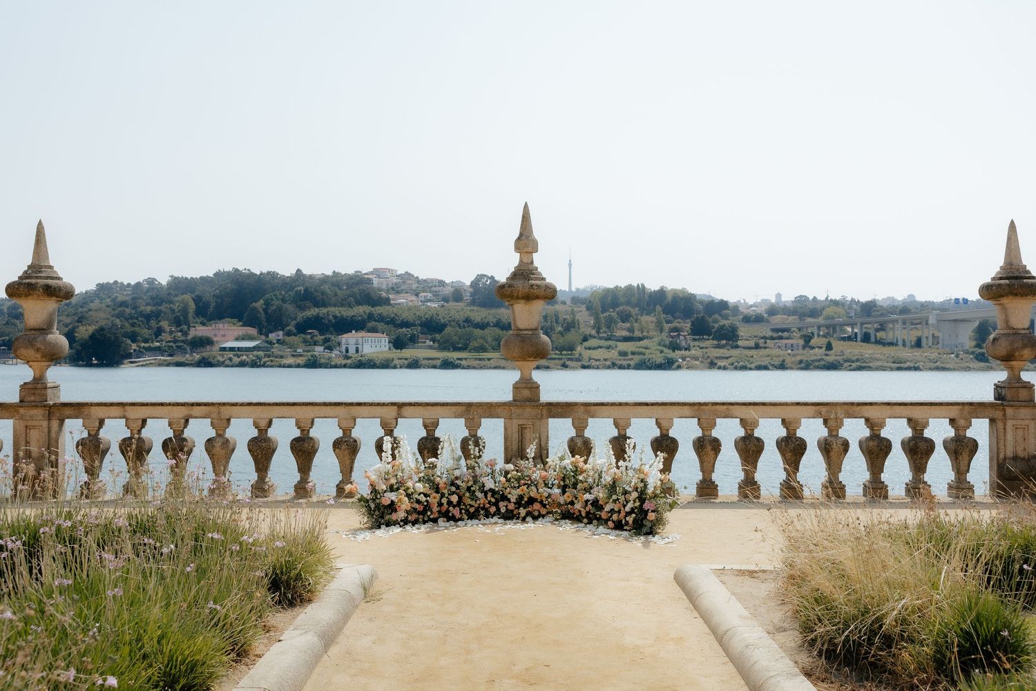 Ornate stone balcony with decorative pillars overlooking a coastal view with dried plants and flowers in Portugal.
