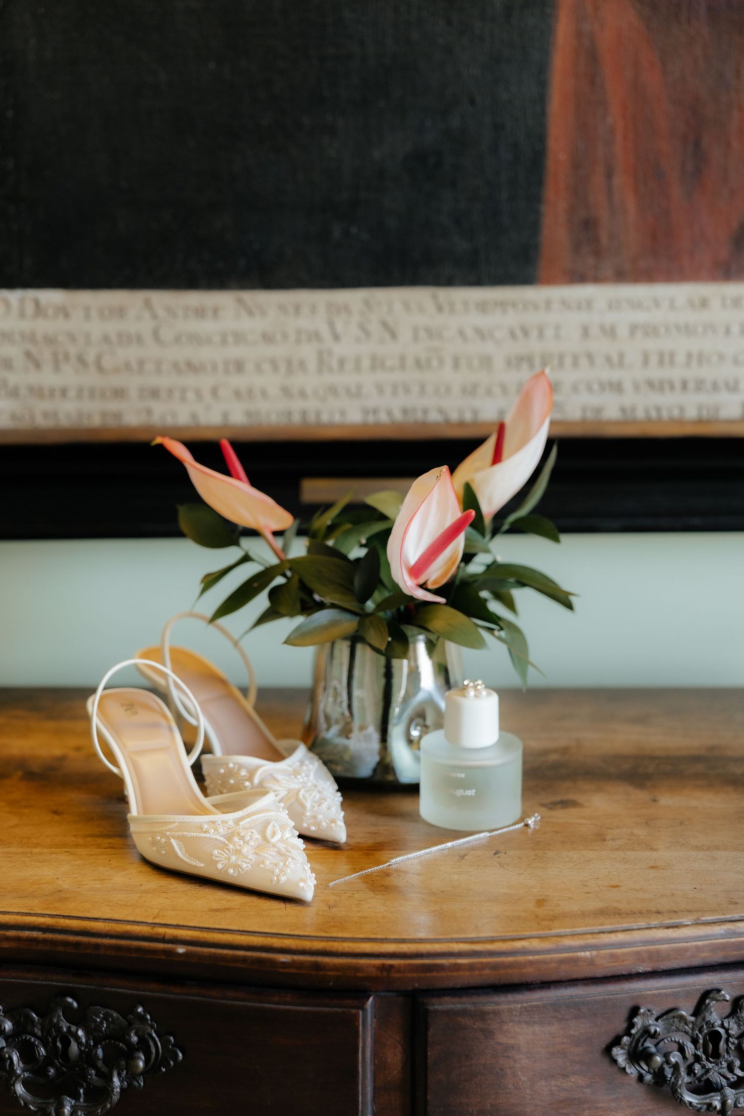 Elegant white lace bridal shoes and pink lily flowers displayed on a rustic wooden table.
