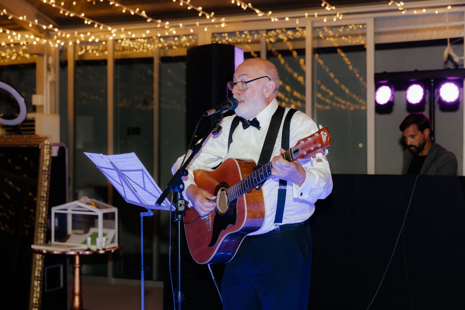A wedding reception dance floor illuminated by string lights and purple uplighting in an indoor venue.