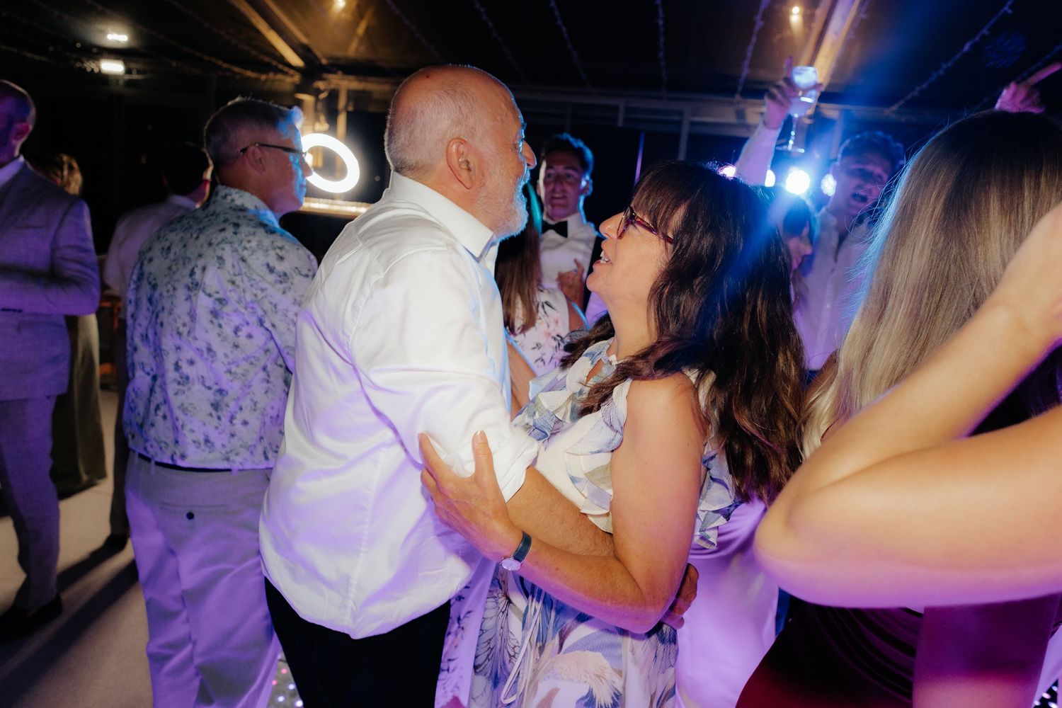 People dancing together on a nightclub dance floor illuminated by purple and blue lighting.