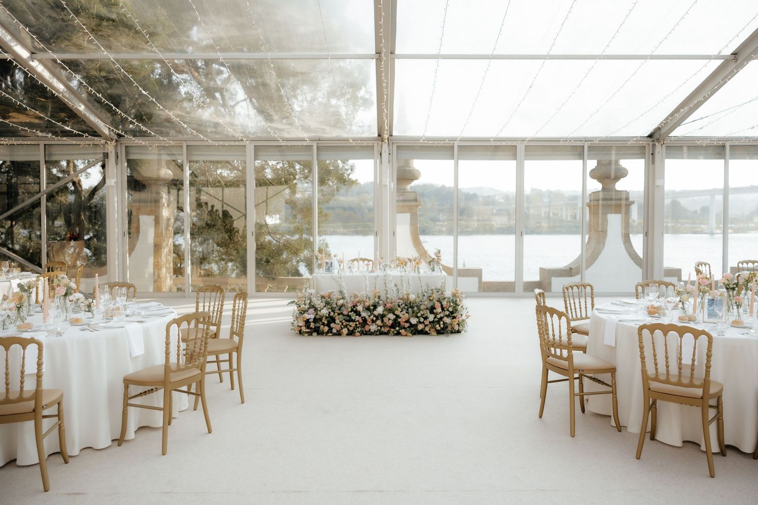 Elegant white wedding reception venue with chiavari chairs and floor-to-ceiling windows overlooking waterfront views.