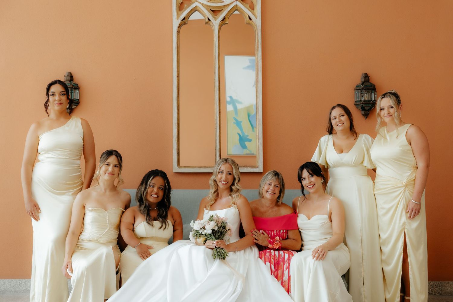 A group of bridesmaids in white dresses stand together holding bouquets during a wedding celebration.