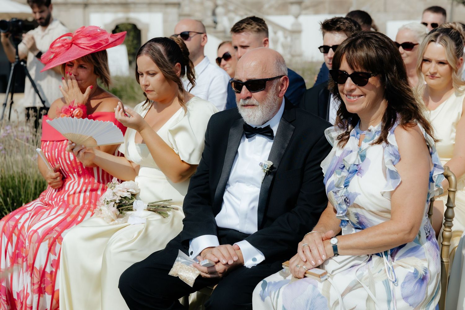 Wedding guests sitting outdoors at a garden ceremony share joyful reactions during the celebration.