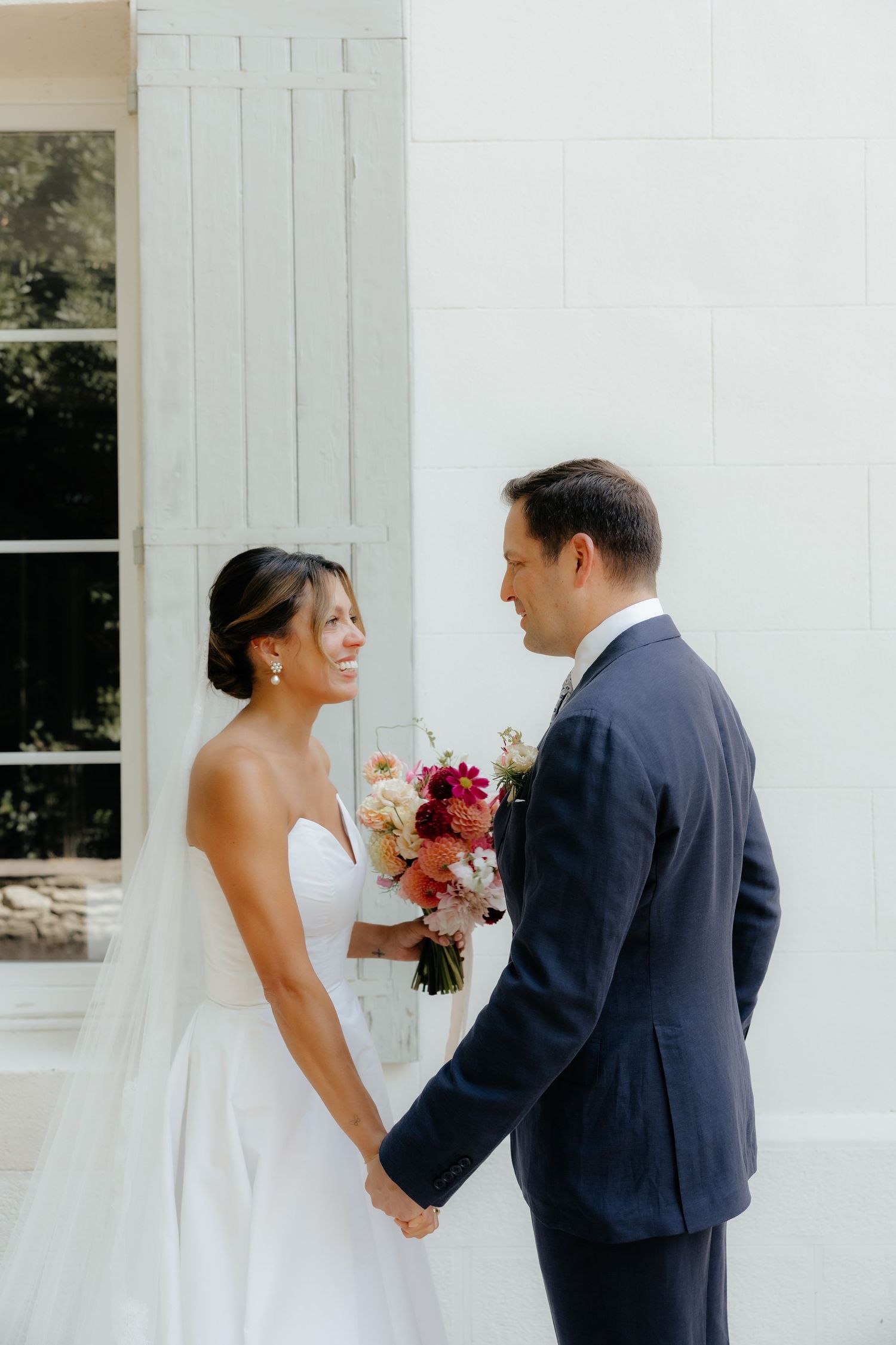Wedding couple sharing a first look moment outside a white building.