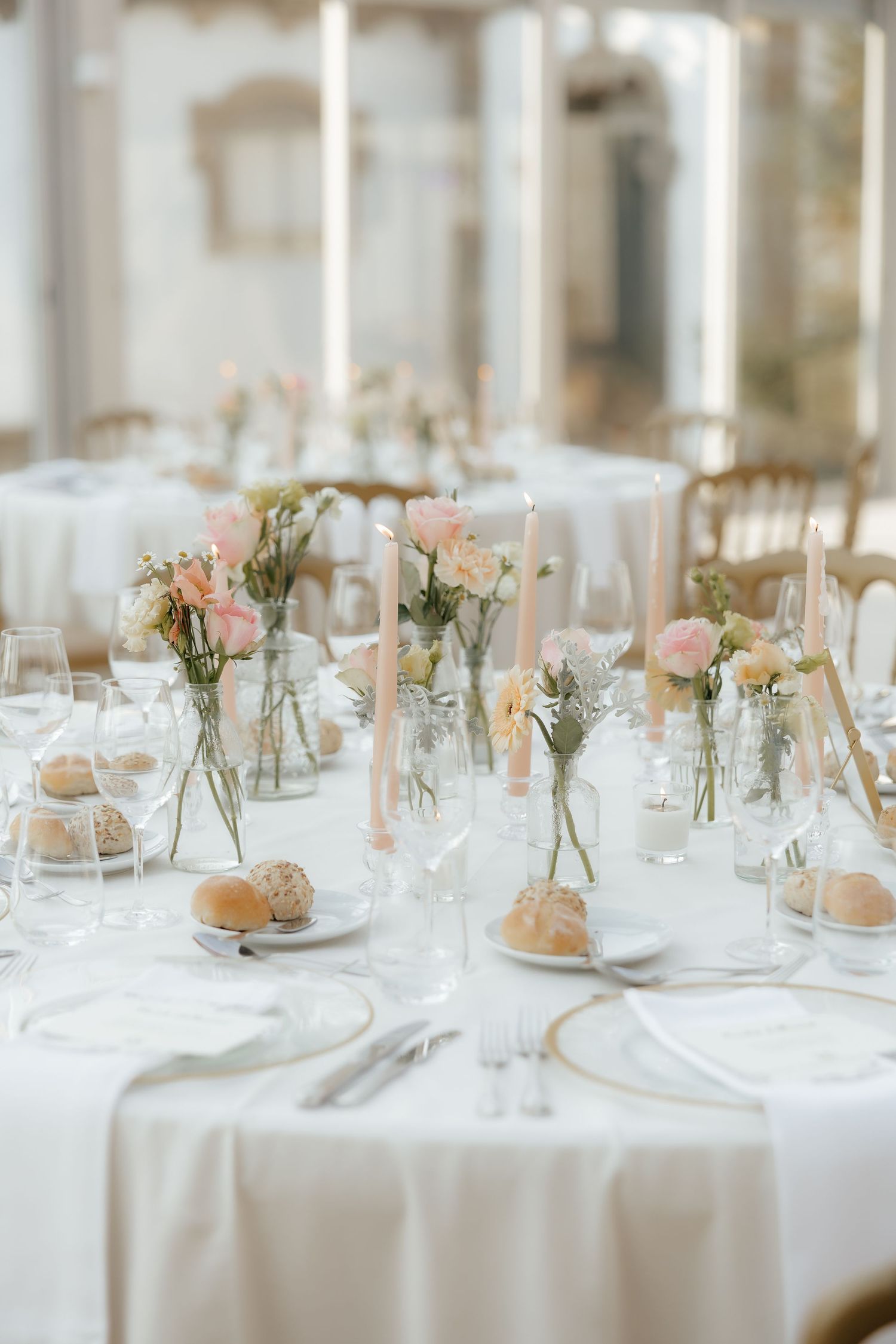 Elegant round wedding reception table with pink roses, taper candles, crystal glassware, and white linens.