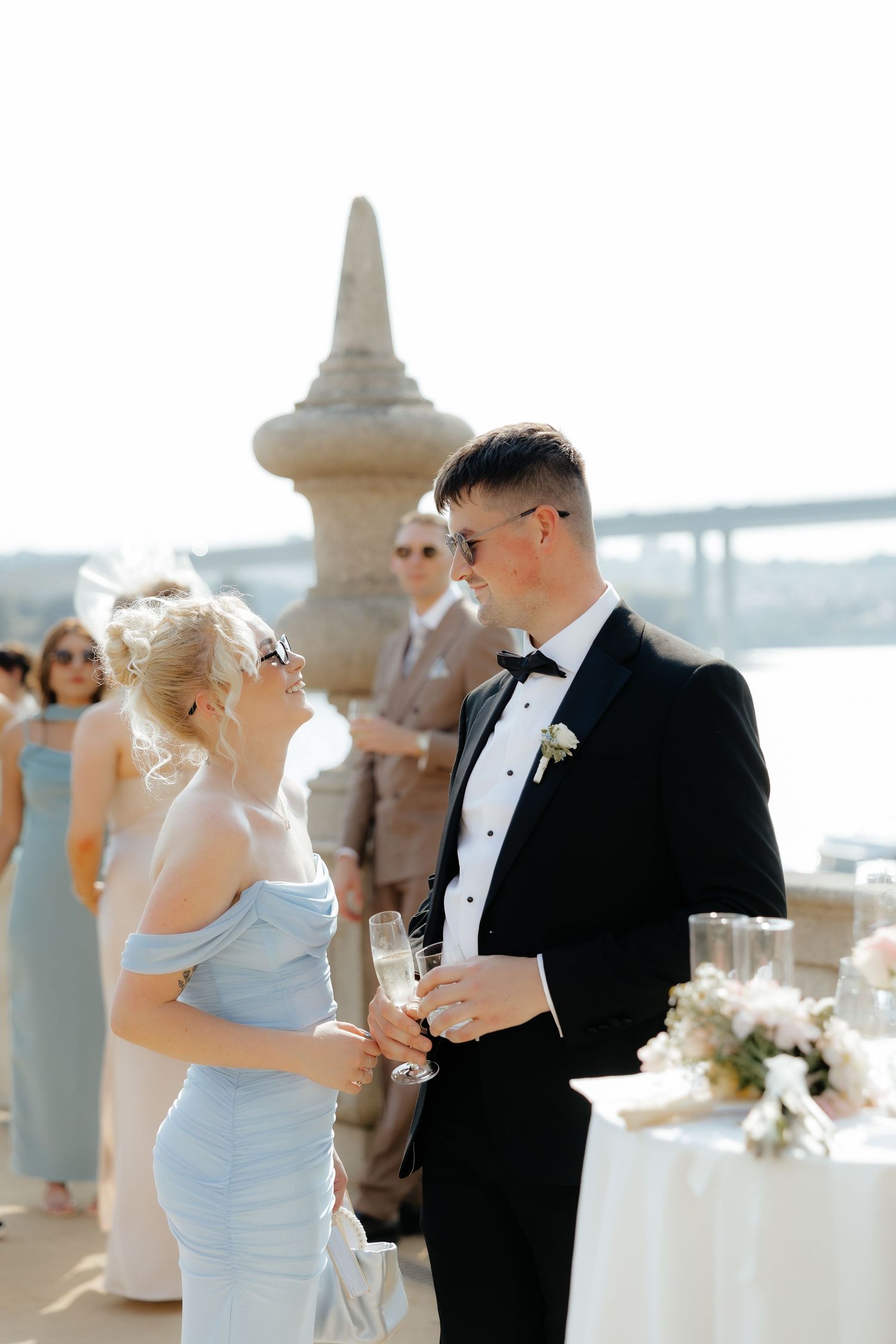 Wedding couple shares a romantic moment during outdoor reception by waterfront venue with elegant decor and guests.