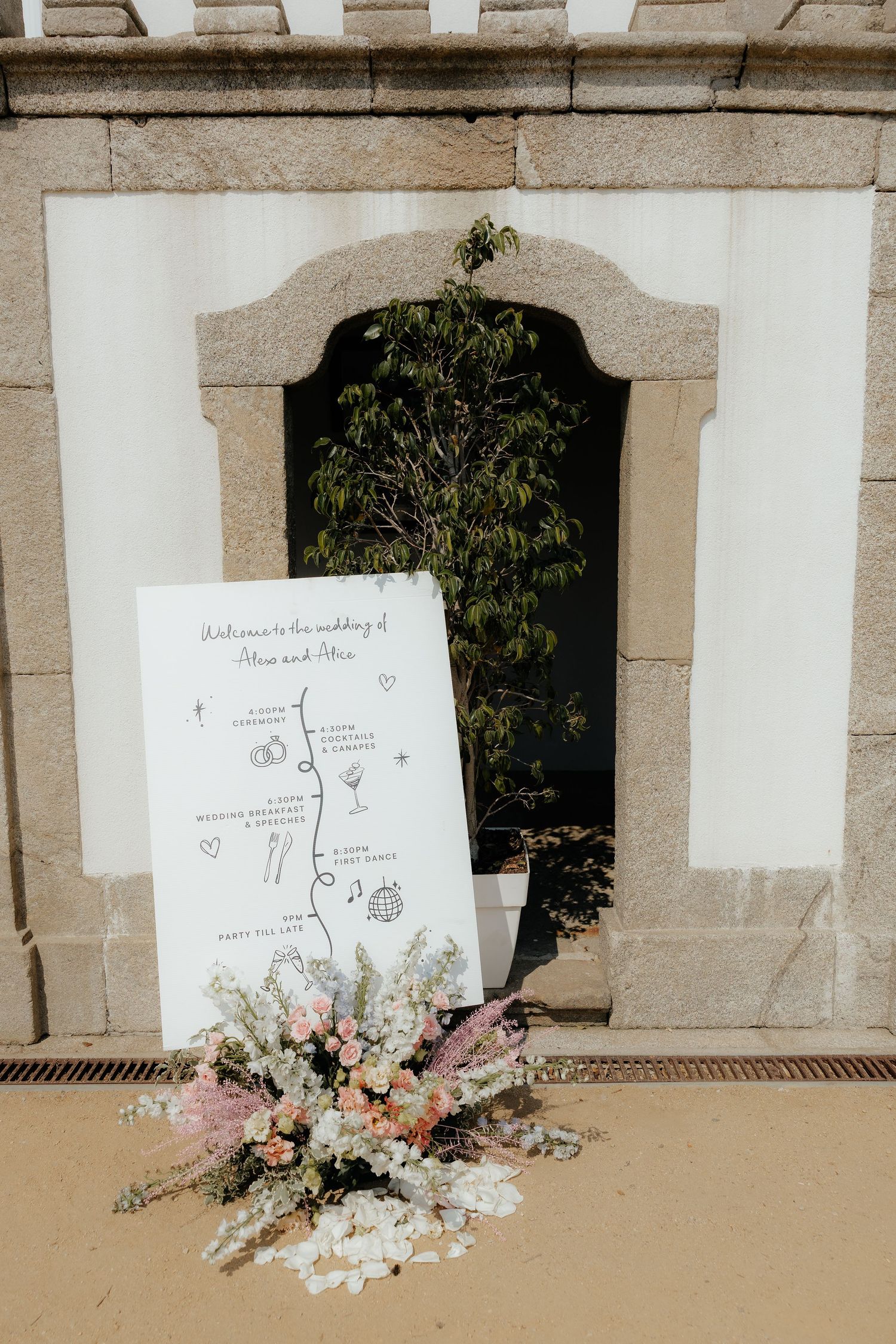 Four wedding ceremony programs displayed on a stone wall with delicate floral arrangements in soft pink and white tones.