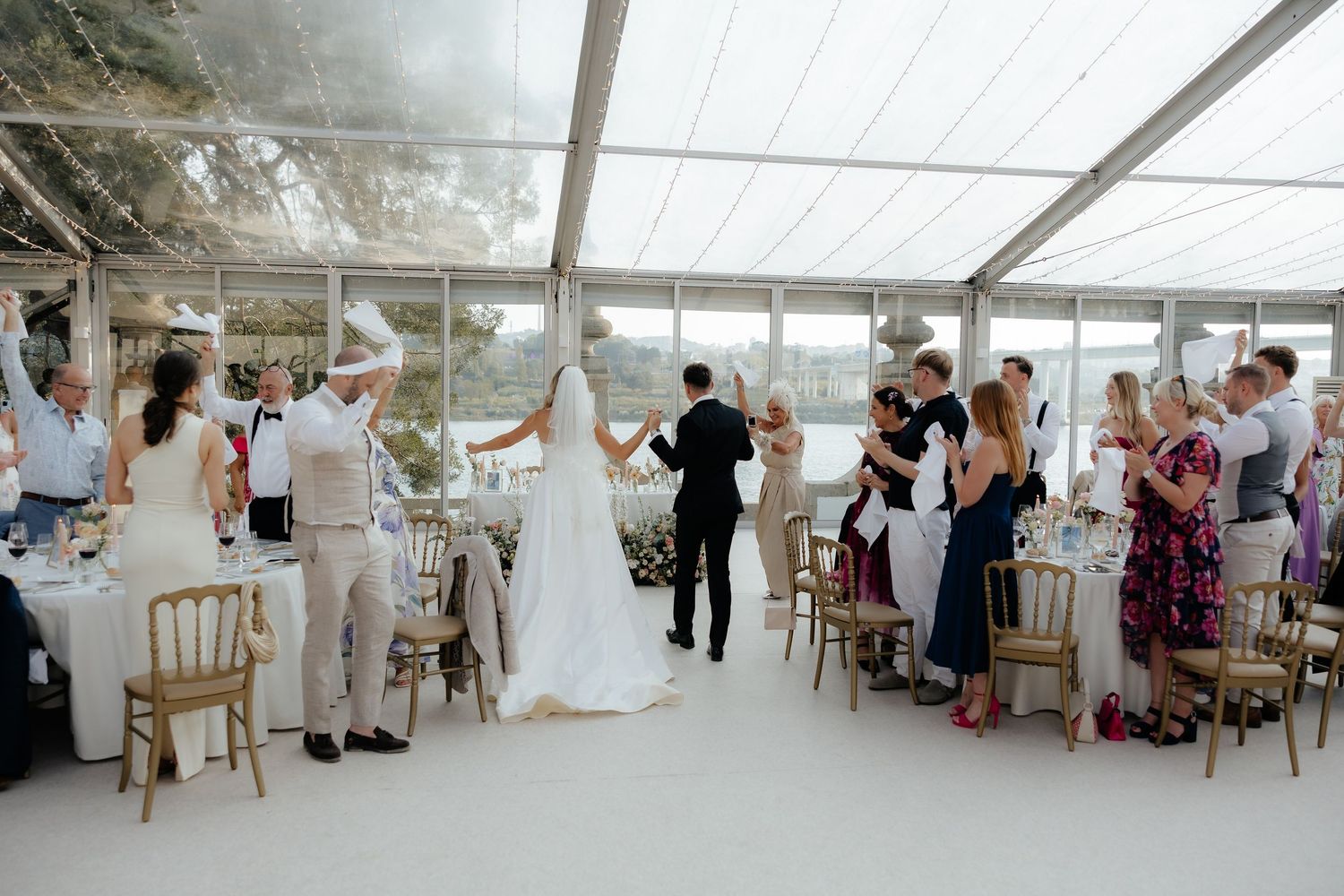 Wedding guests seated at round tables inside an elegant white marquee reception tent with hanging decorations.