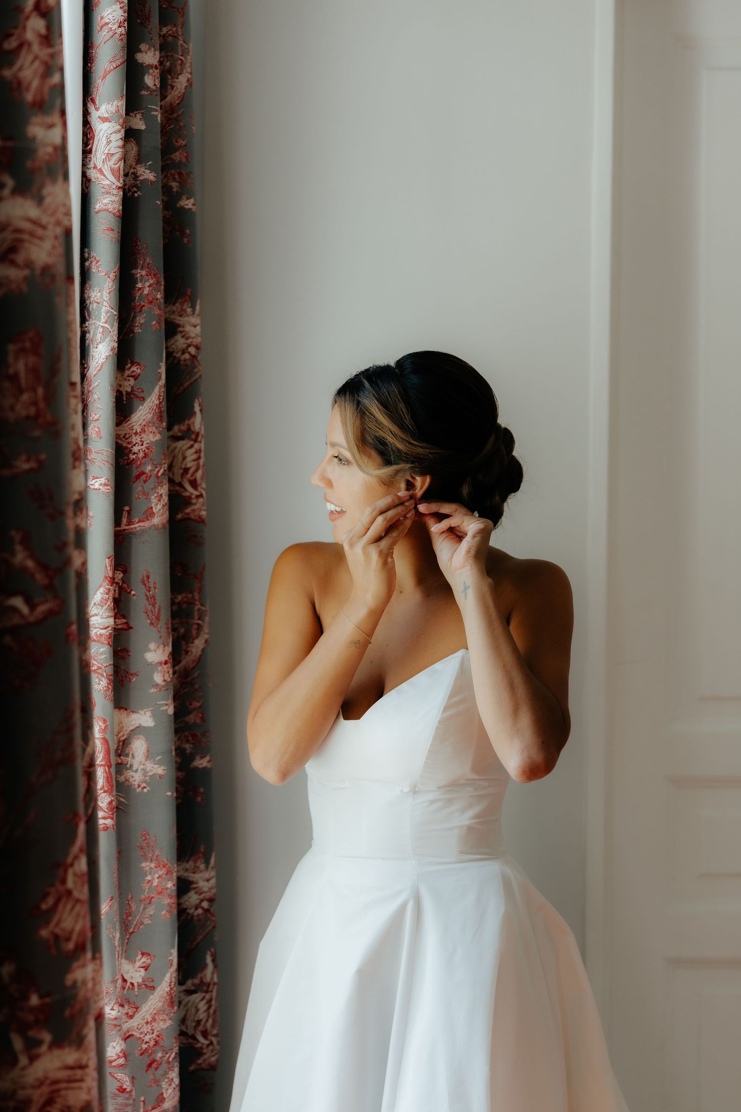 Getting ready scene with someone in a white dress against floral curtains.
