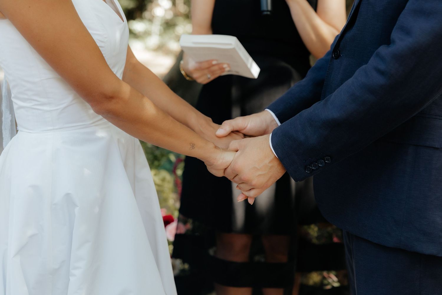 Close-up of couple holding hands during outdoor wedding ceremony.