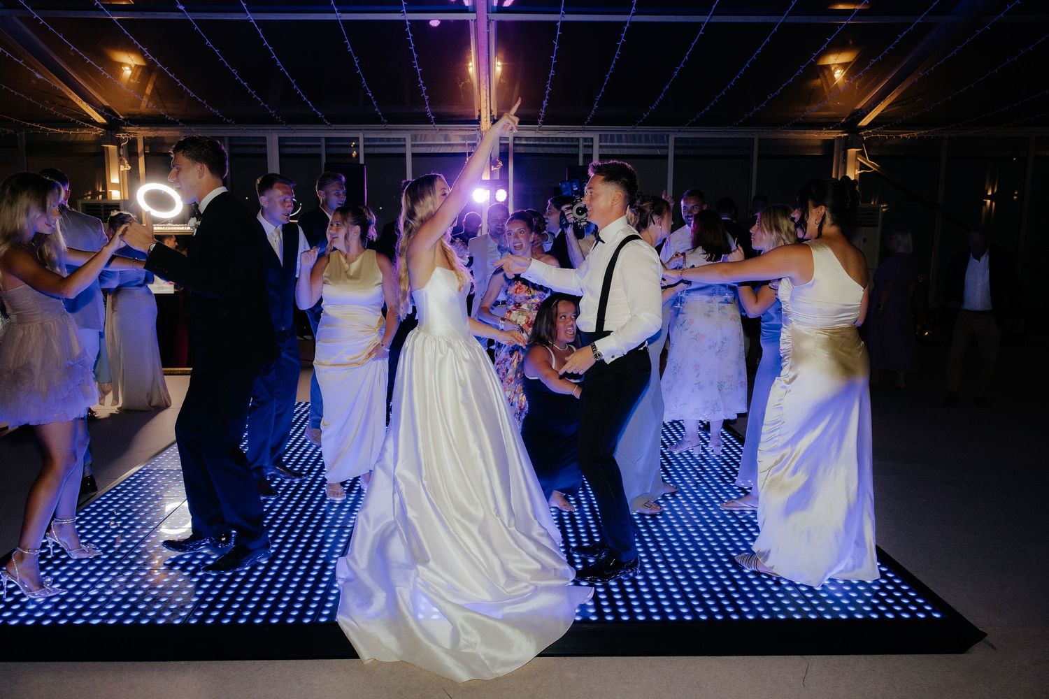 Couples dance together on an illuminated dance floor at a wedding reception with purple lighting effects.