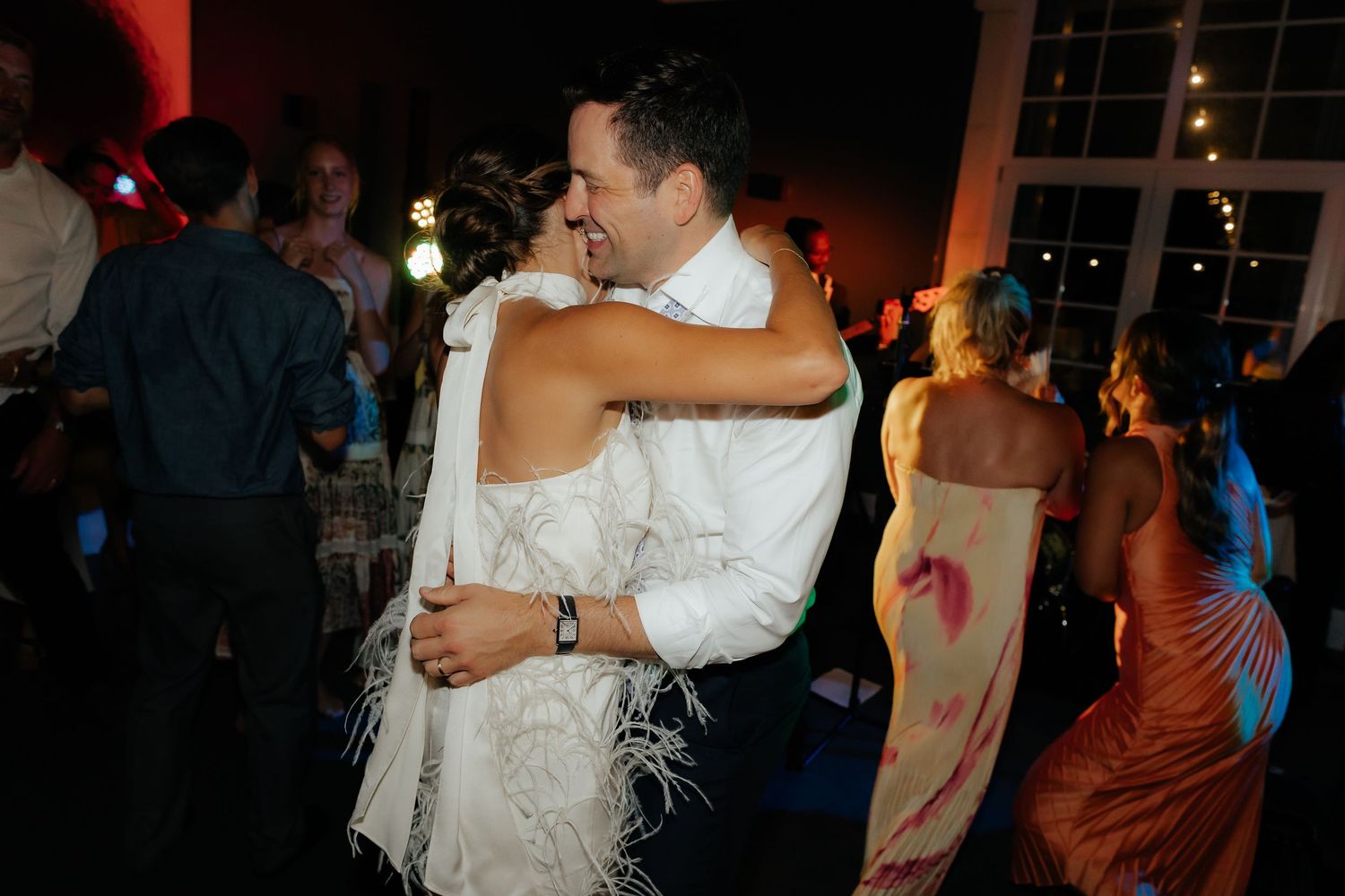 Couples dancing together at a dimly lit wedding reception with festive lighting in the background.