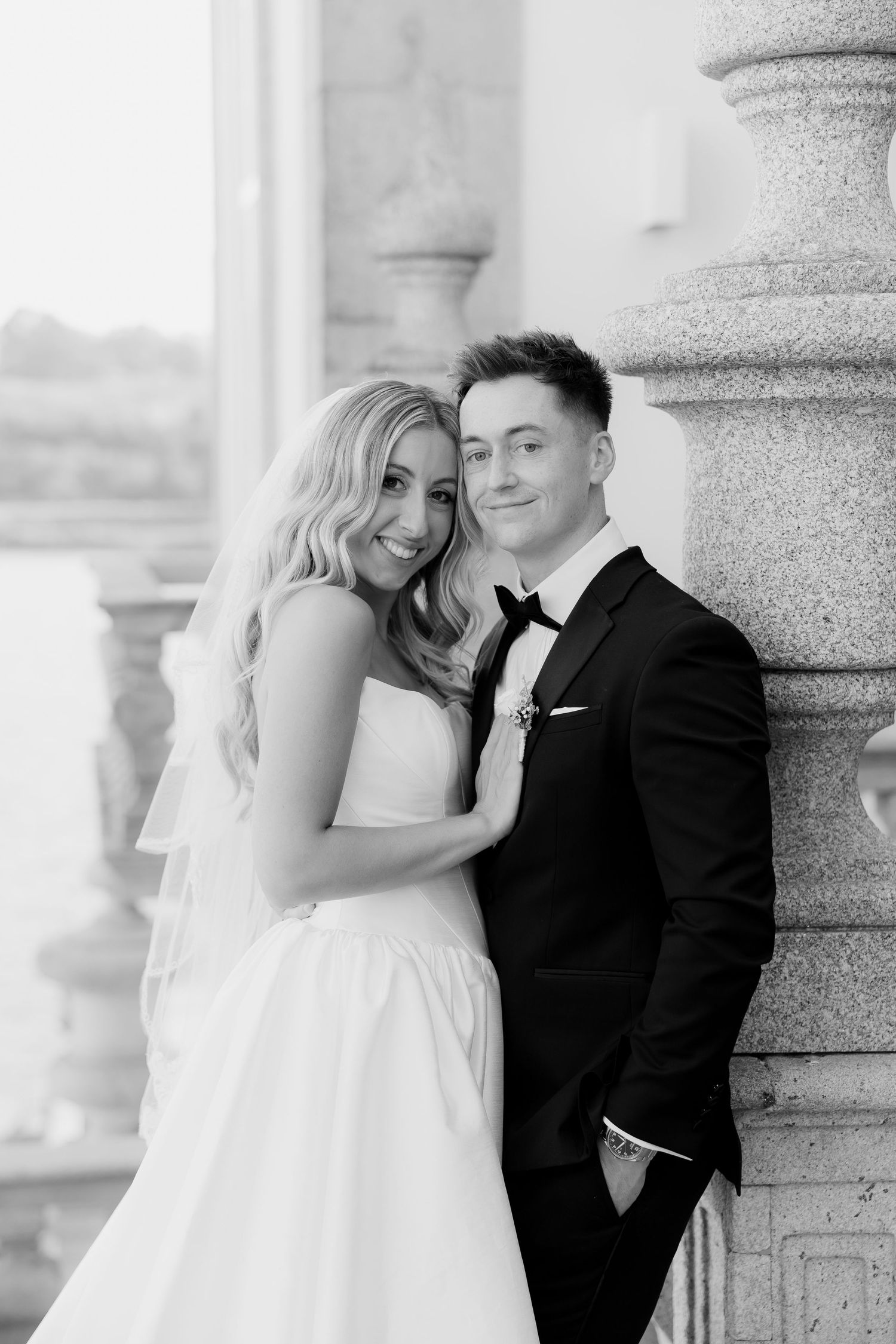A romantic black and white wedding photo series showing tender moments between newlyweds against elegant stone columns.
