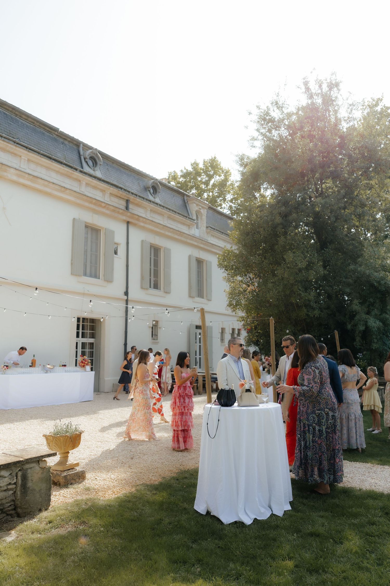 Wedding reception setup with white tablecloths and decorations outside a white building.