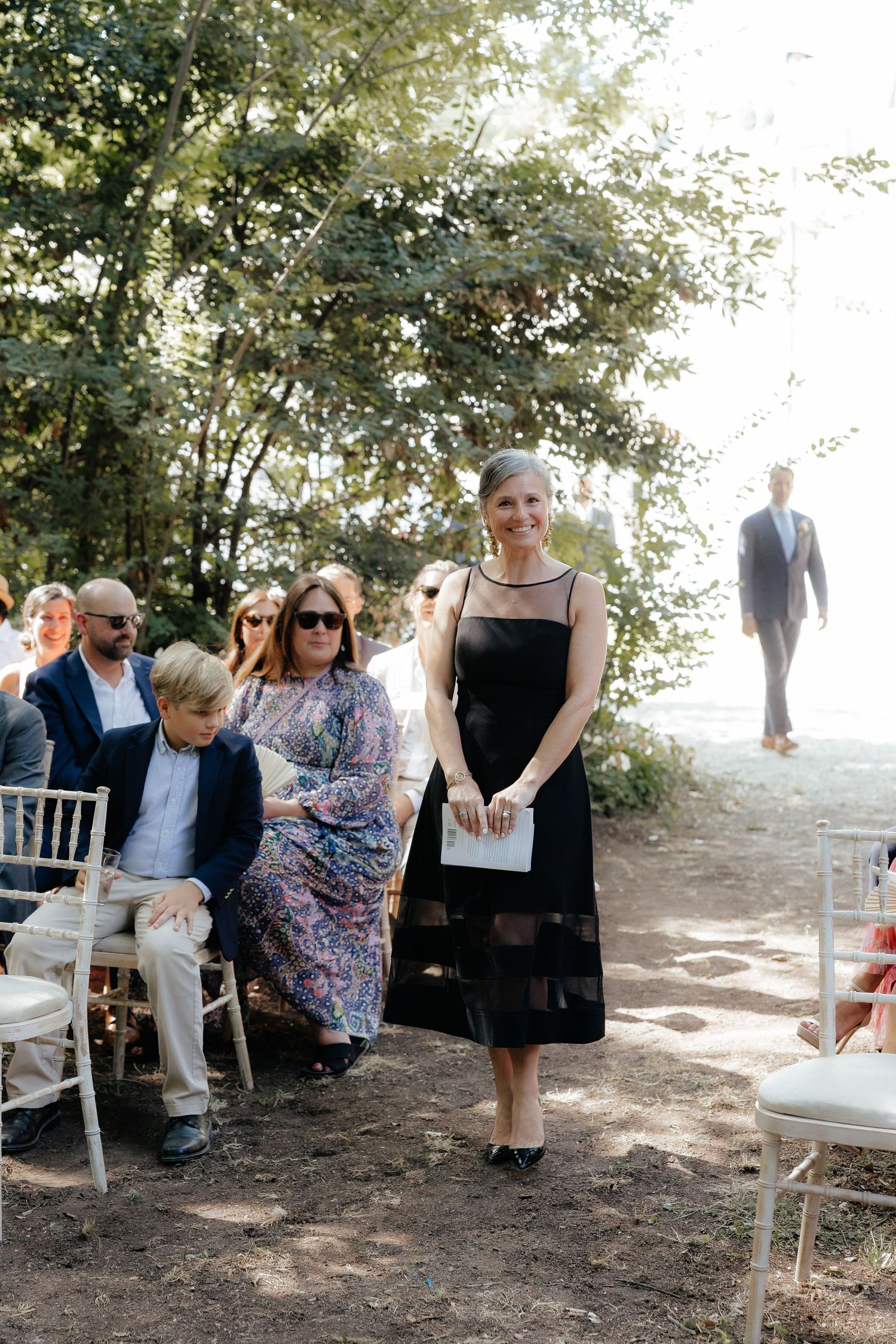 Wedding guests seated on white chairs during an outdoor ceremony.