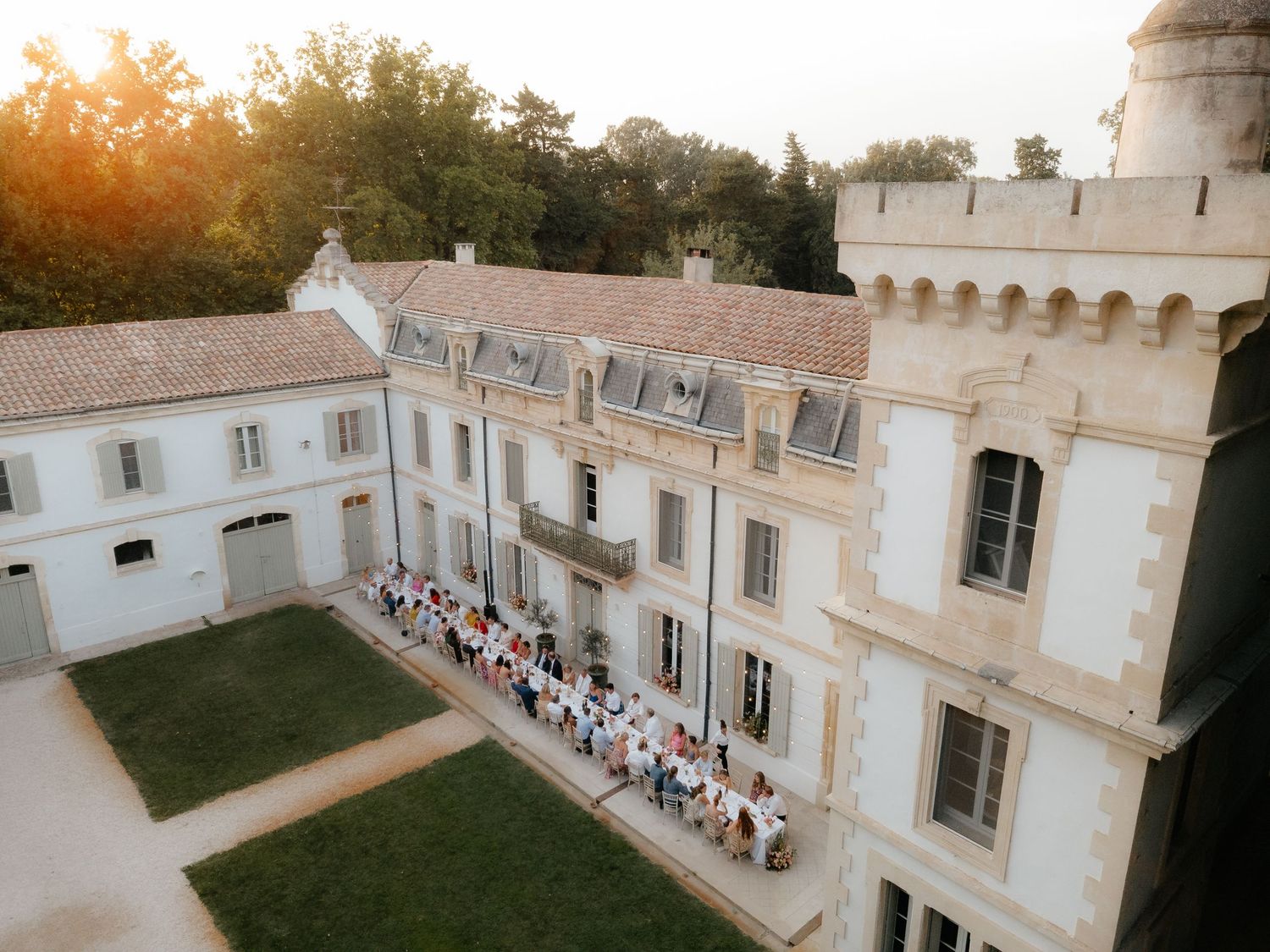Panoramic view of wedding guests seated in rows outside a historic white Mediterranean-style building at sunset.
