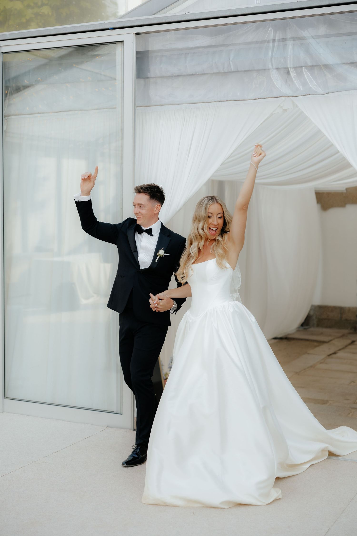 Newlywed couple in formal attire dancing and celebrating together in an elegant white room.