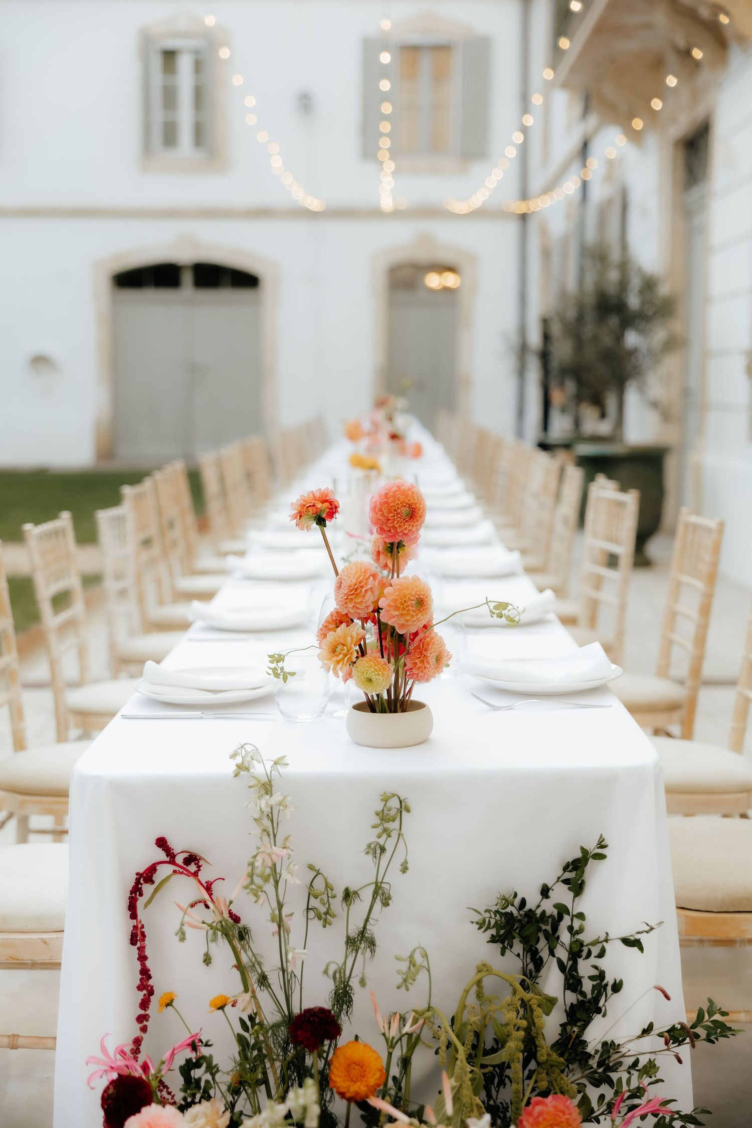 Elegant wedding reception table with white linens and orange floral centerpieces in a bright indoor venue.