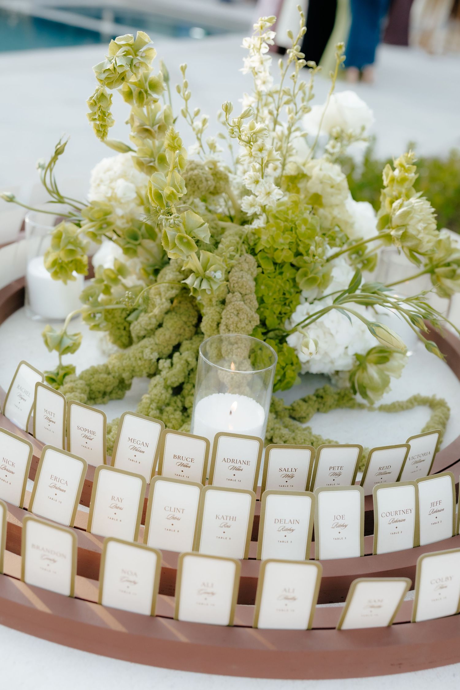 Elegant wedding escort card display arranged in circular tray with white and green floral centerpiece.