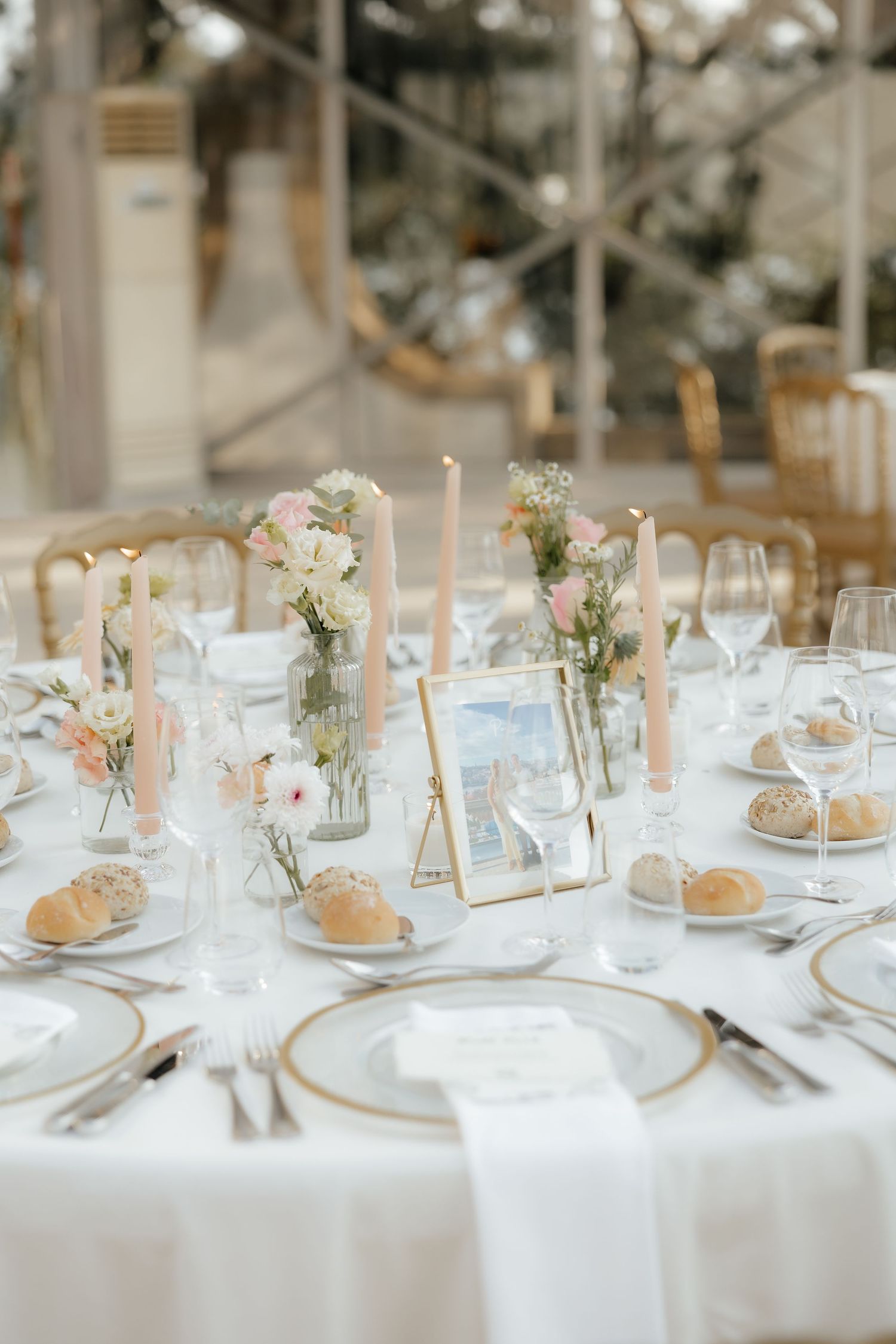 Elegant wedding reception table settings with delicate floral centerpieces, white linens, and gold table numbers.