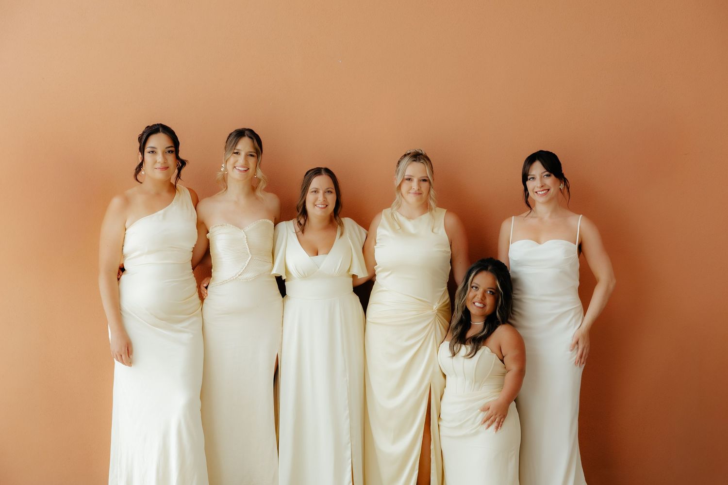 A group of people wearing white wedding dresses stand together in a row for a formal photograph.