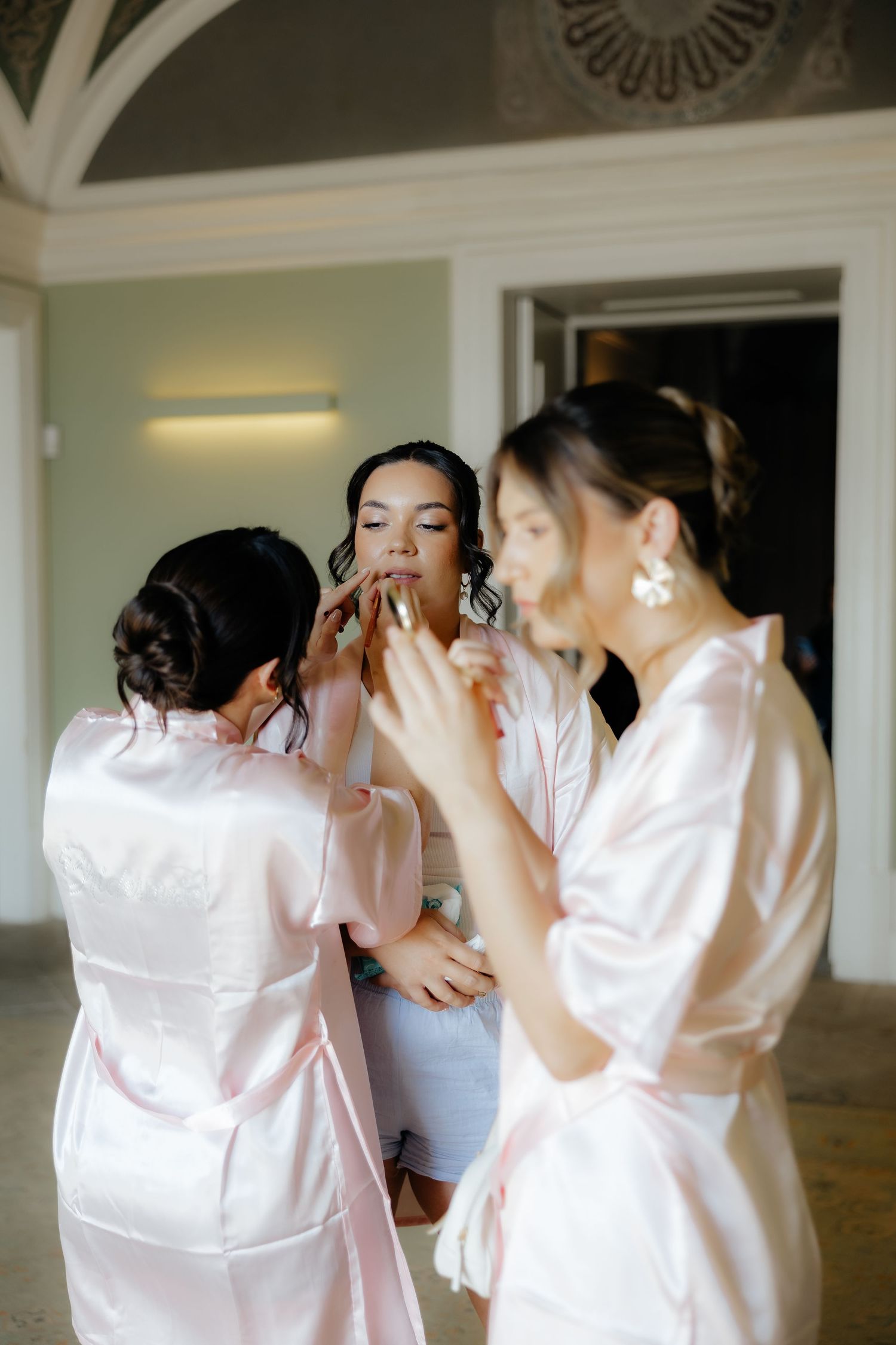 A group in matching pink silk robes getting ready together in a bright room before a special event.