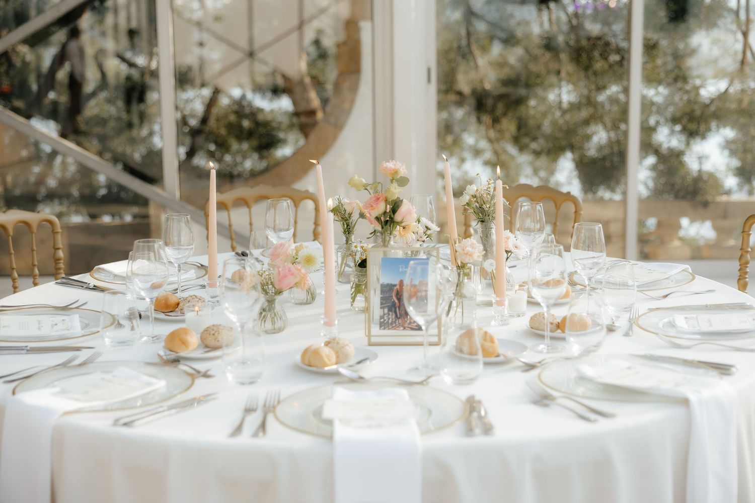 Sophisticated wedding table centerpiece featuring pastel flowers, tall candles, framed table number, and crystal glasses.