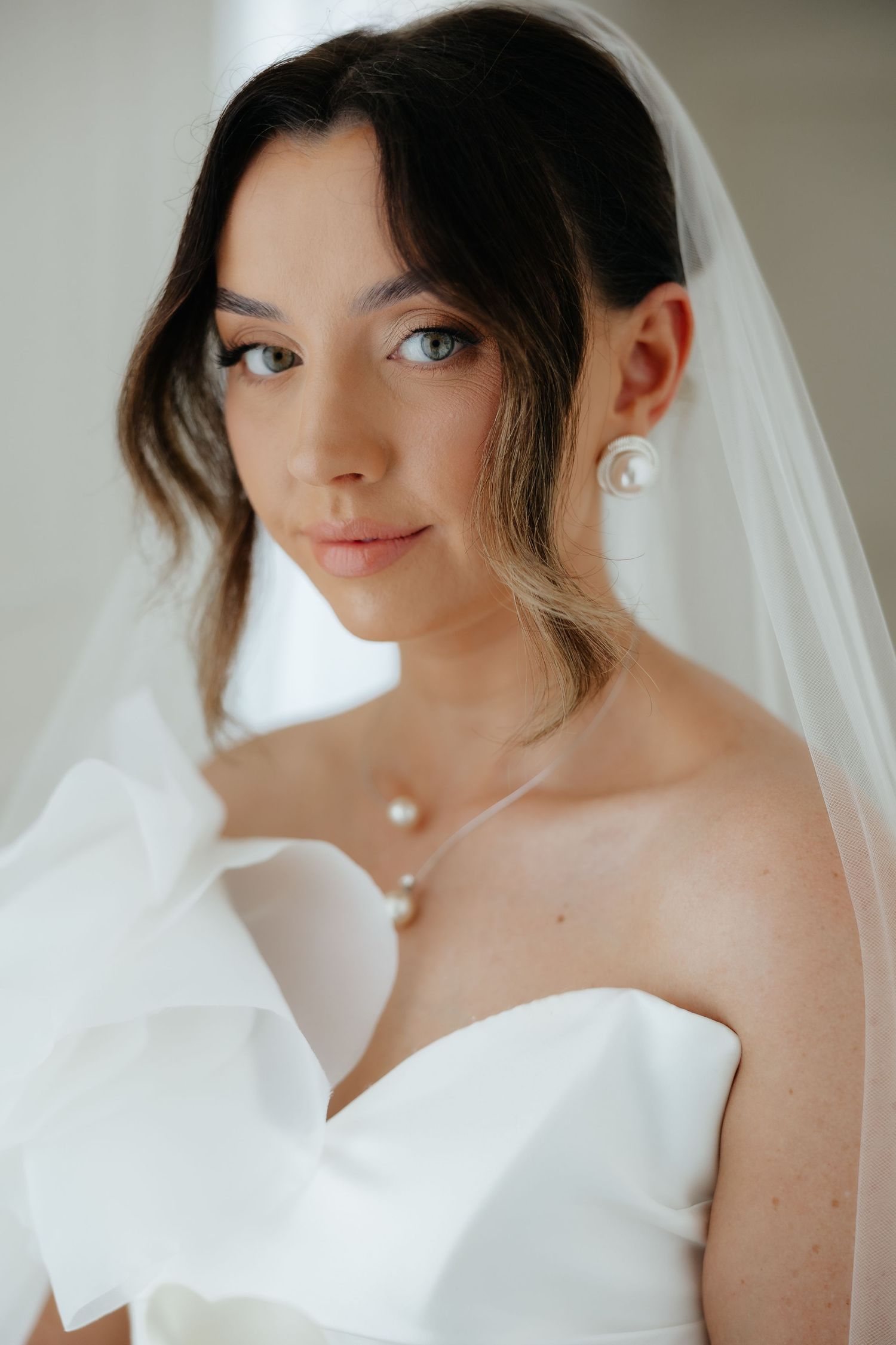Elegant bride wearing a white strapless gown, pearl jewelry, and a veil, posing for a classic bridal portrait.
