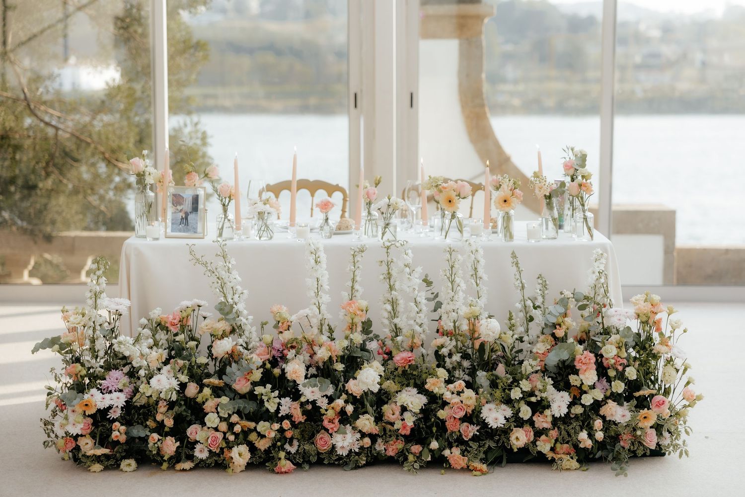 Long floral table arrangement with peach and white blooms decorates an elegant wedding reception by the waterfront.