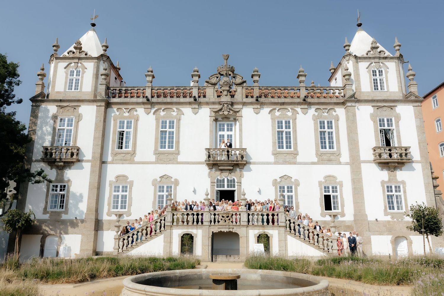Ornate white baroque palace with twin towers and grand staircase stands in Portugal against blue sky.