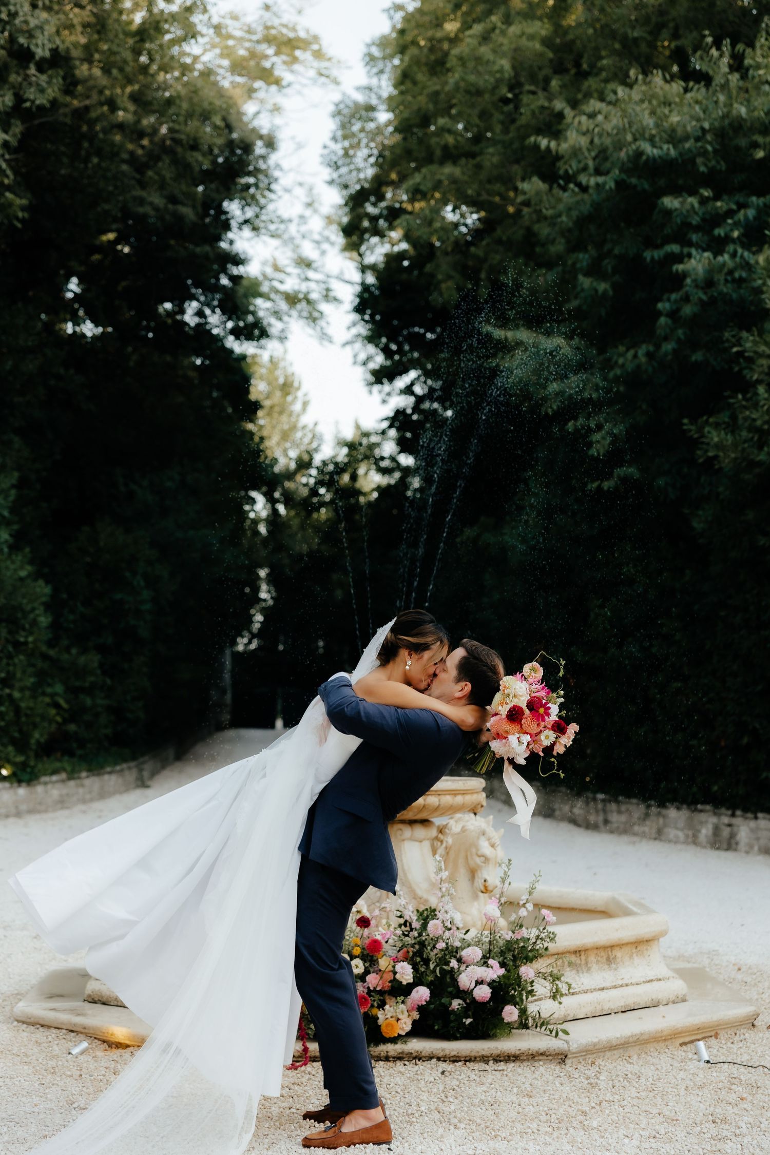 Romantic wedding couple sharing a moment on a gravel path surrounded by trees.