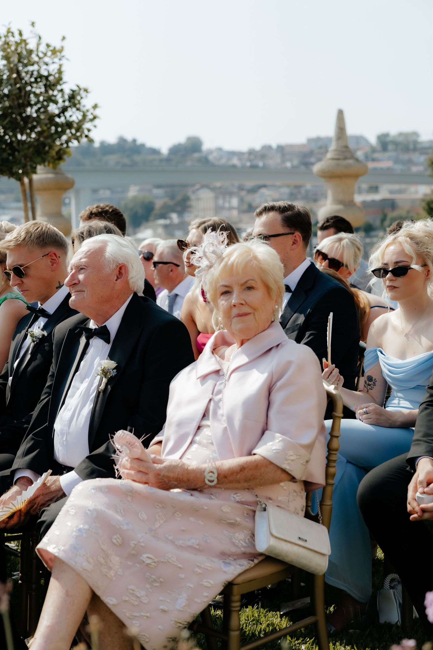A crowd of formally dressed people gathered outdoors for an event on a sunny day.