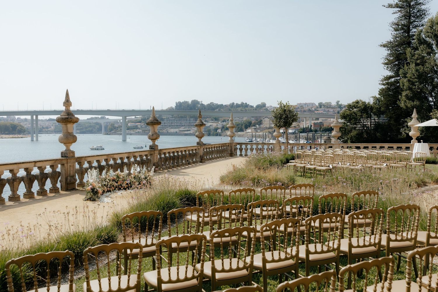 Elegant wedding ceremony setup with white chairs and floral arrangements along a waterfront terrace overlooking the bay.