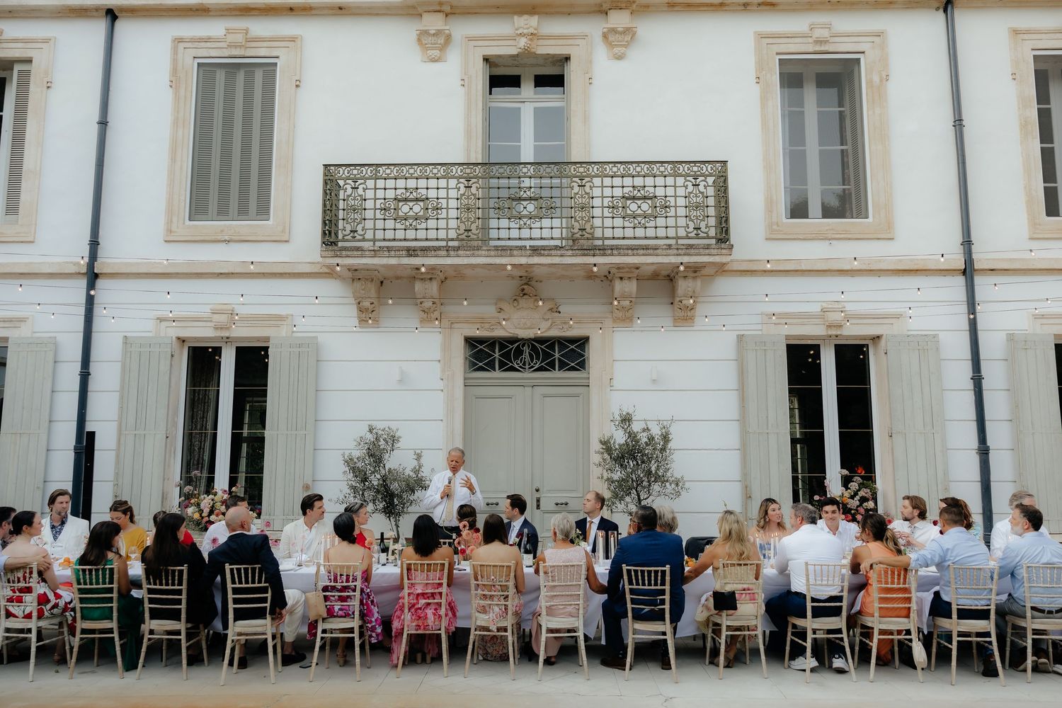 Outdoor restaurant patio with wooden chairs and tables arranged along a white building facade.