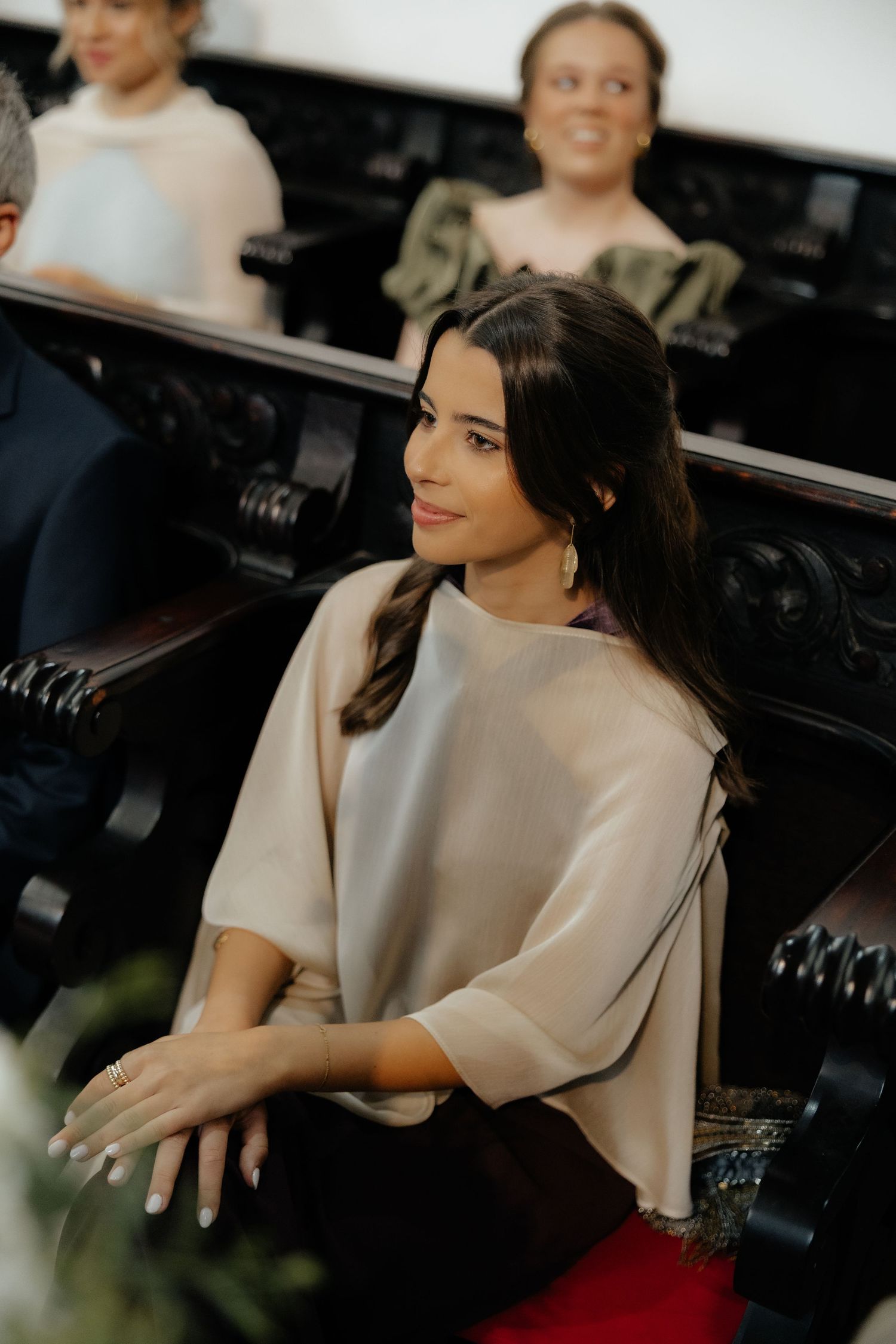 Beautiful brunette woman in beige top sits in church pew at wedding ceremony.