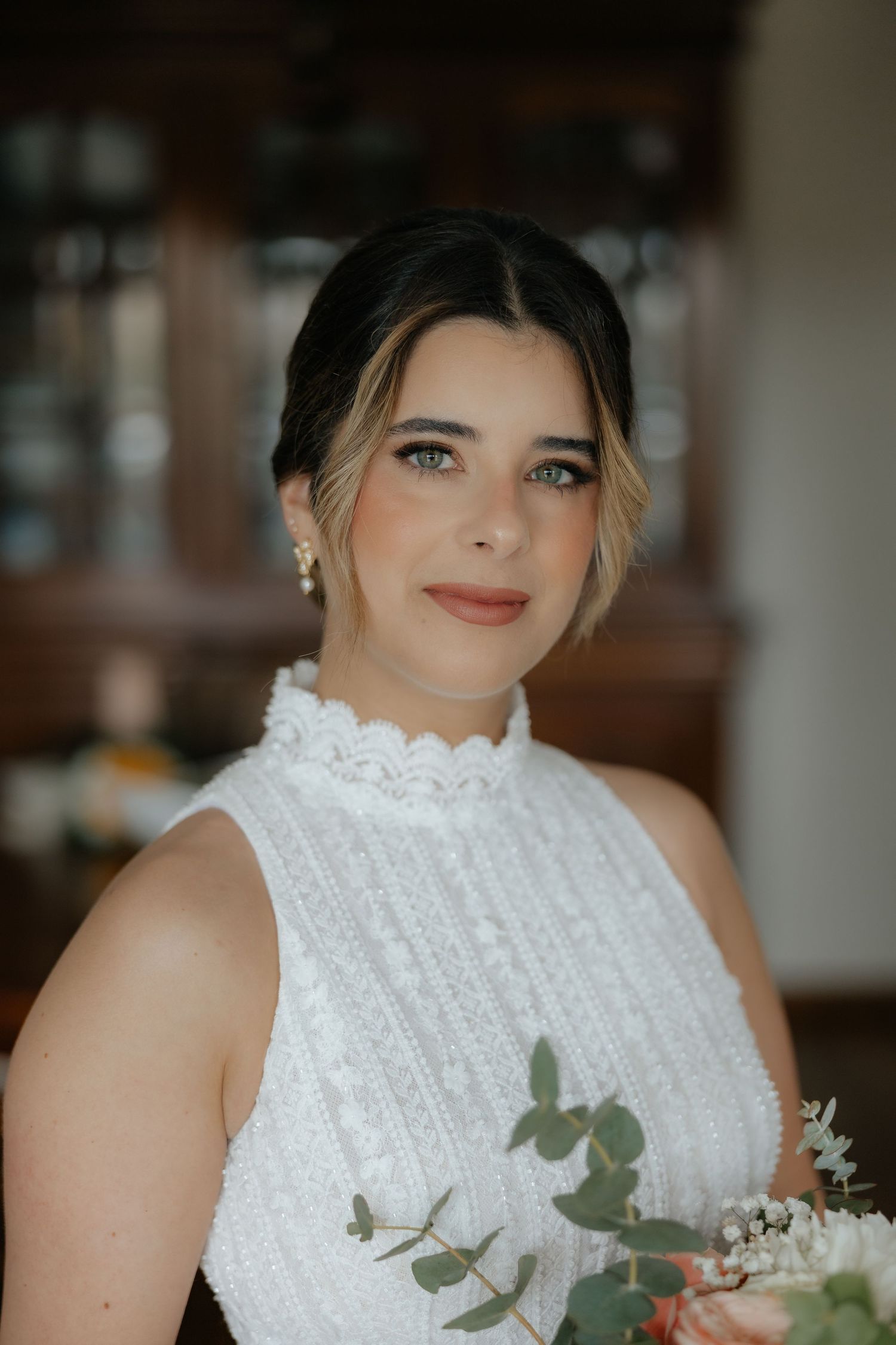 Close-up portrait of a beautiful bride in a white lace high-neck gown holding a bouquet.