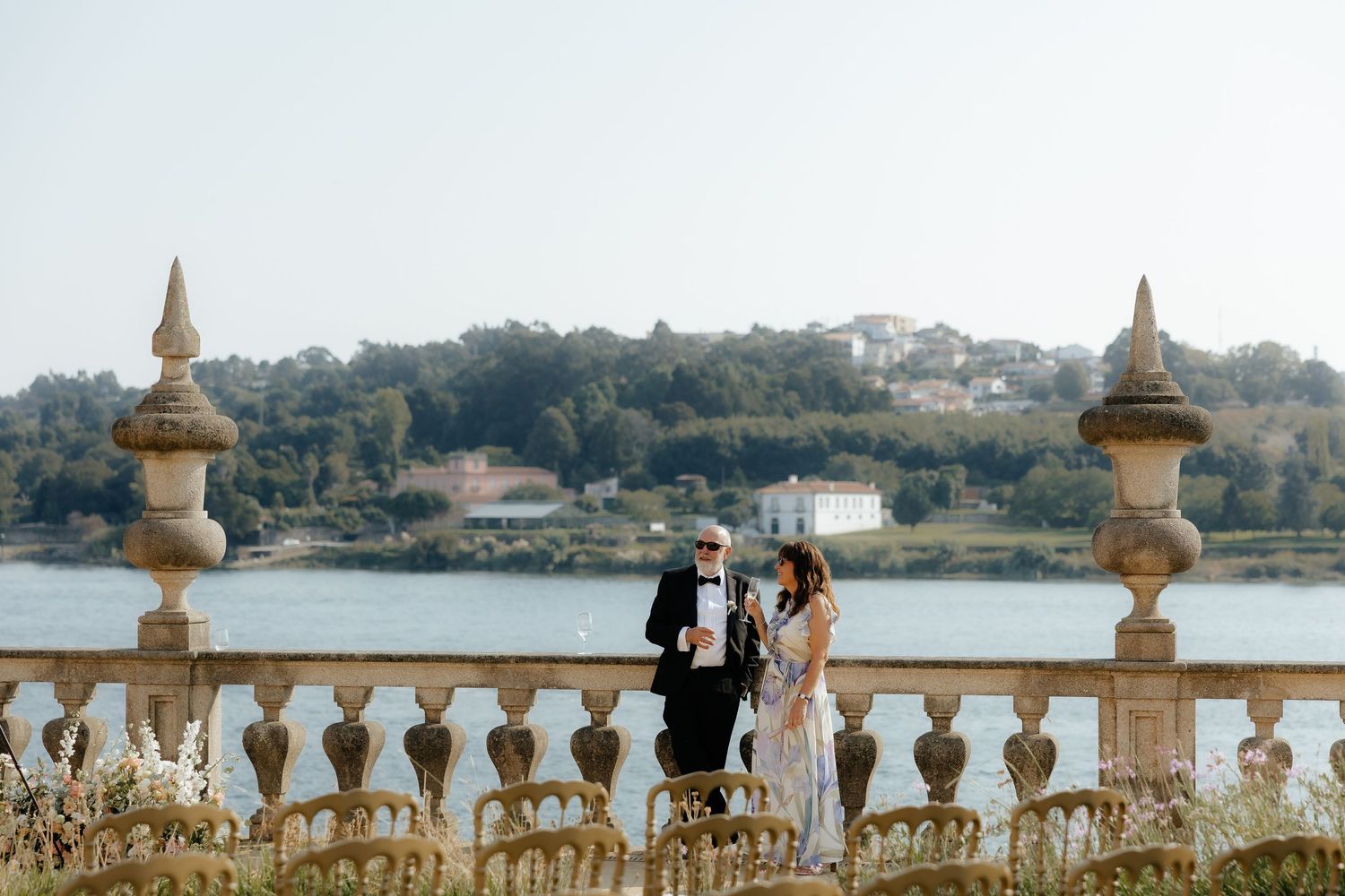 A panoramic view of a stone balustrade overlooking a scenic lake with trees and buildings in the distance.