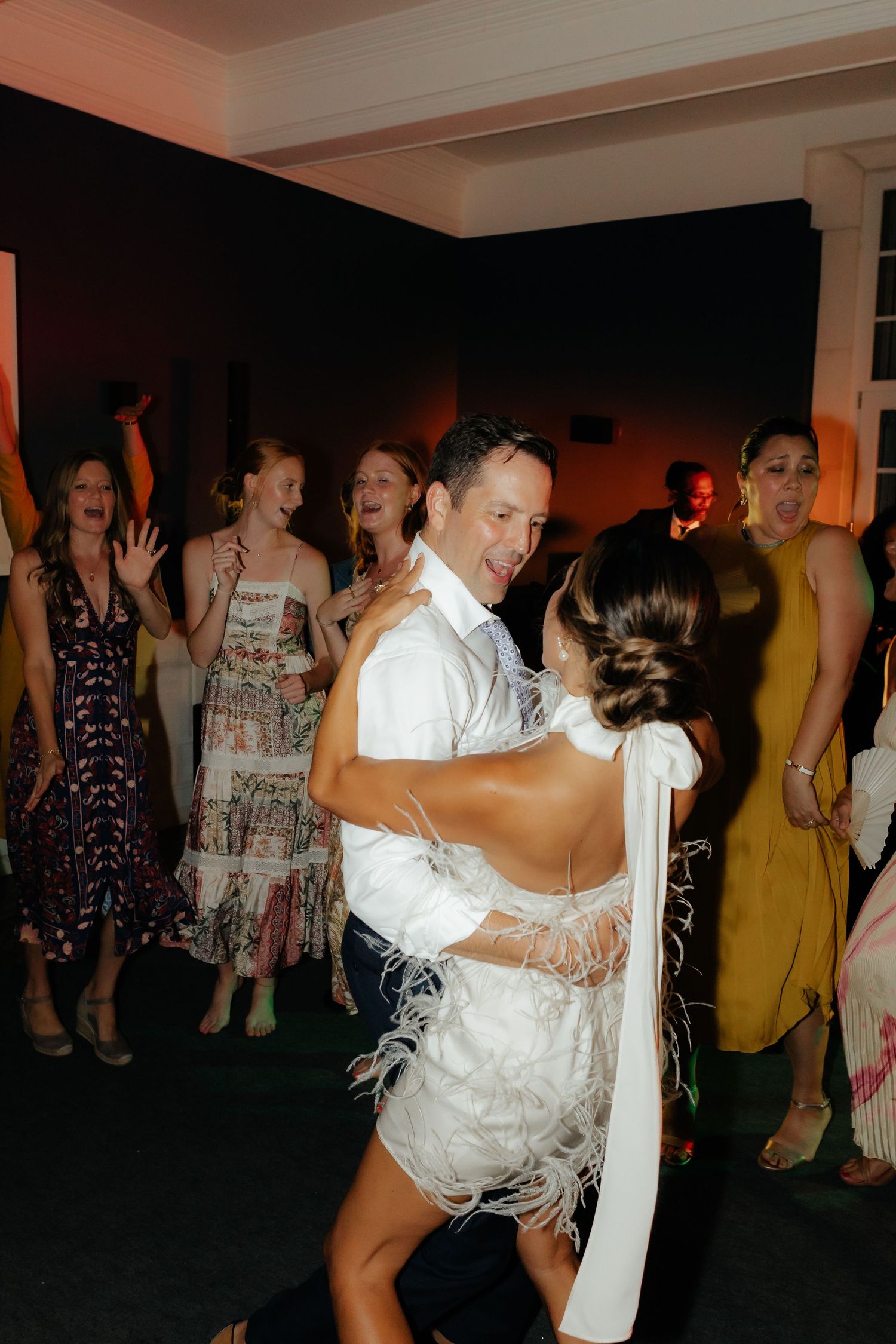 Wedding reception dance floor with guests dancing and celebrating in an indoor venue with white decor.