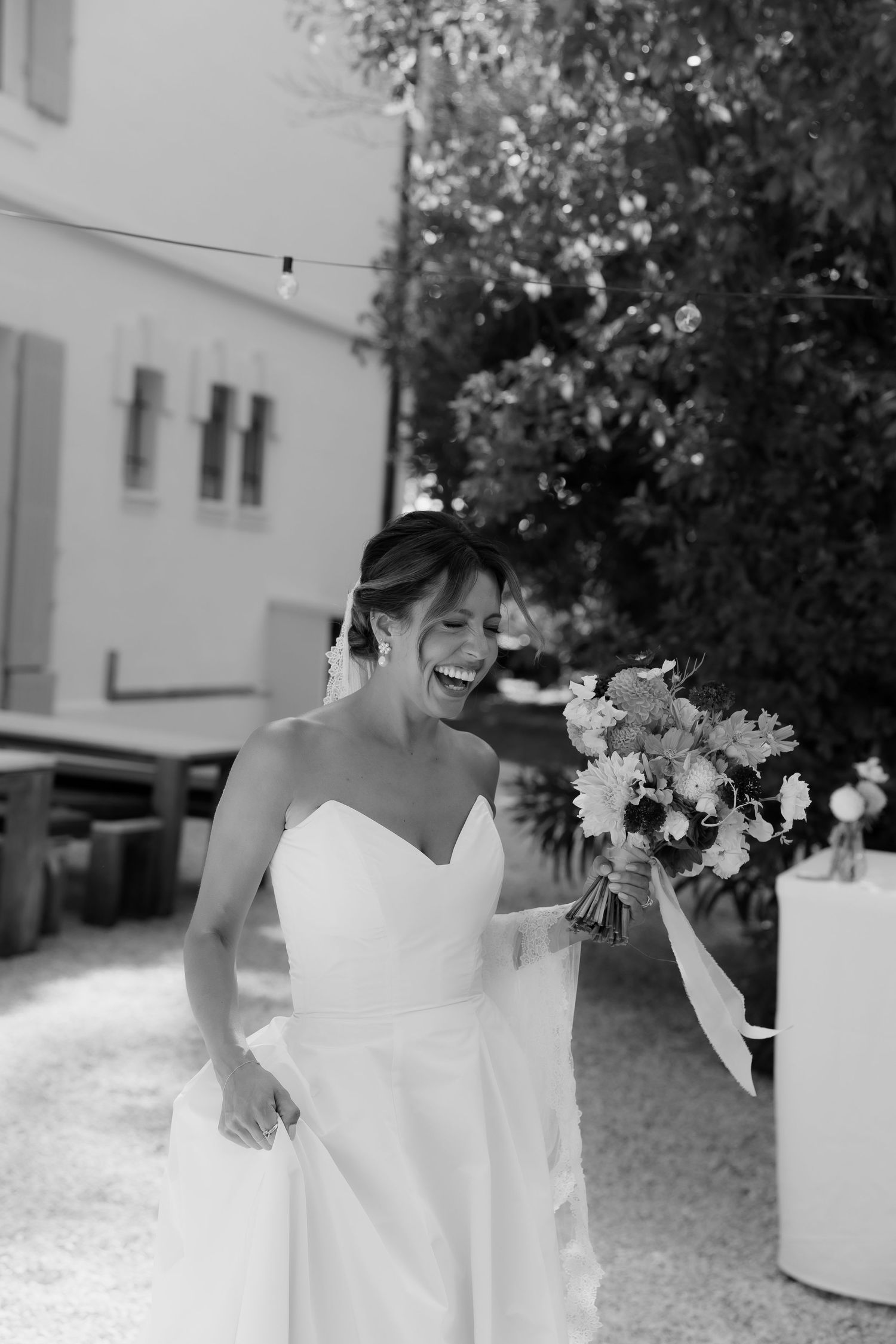 A bride in a white wedding dress holds a bouquet during an outdoor celebration.
