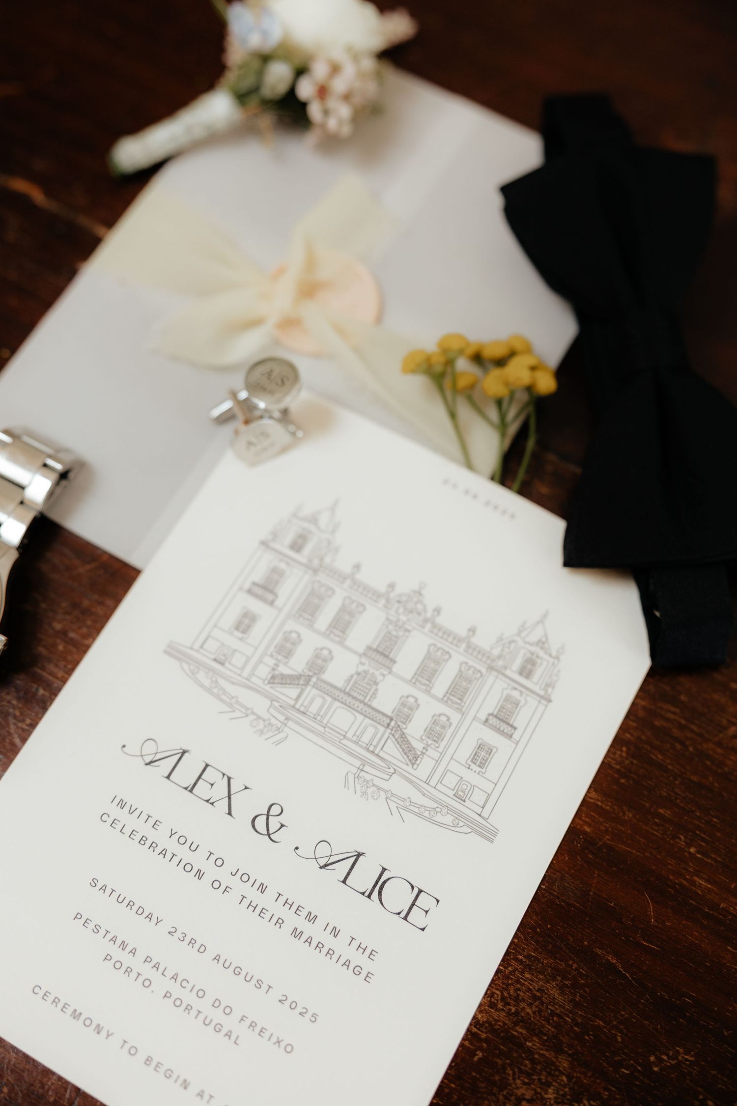 Elegant wedding invitation suite featuring a delicate architectural sketch of a building and white floral details on dark wood.