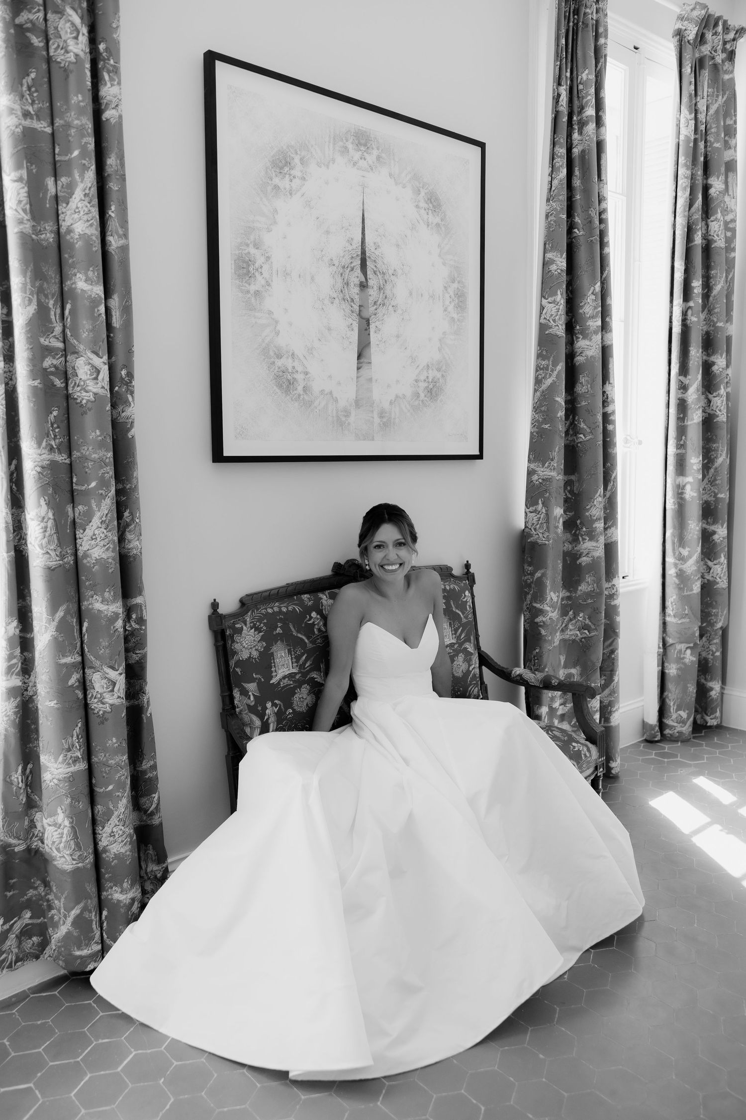White wedding dress with flowing skirt photographed against floral curtains in black and white.