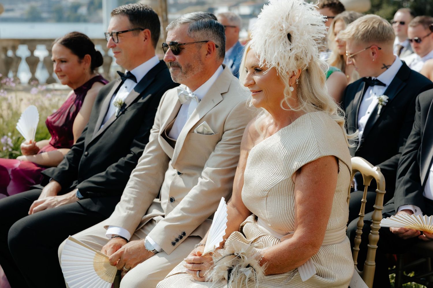 Wedding guests seated in rows at an outdoor ceremony listen attentively during a daytime celebration.