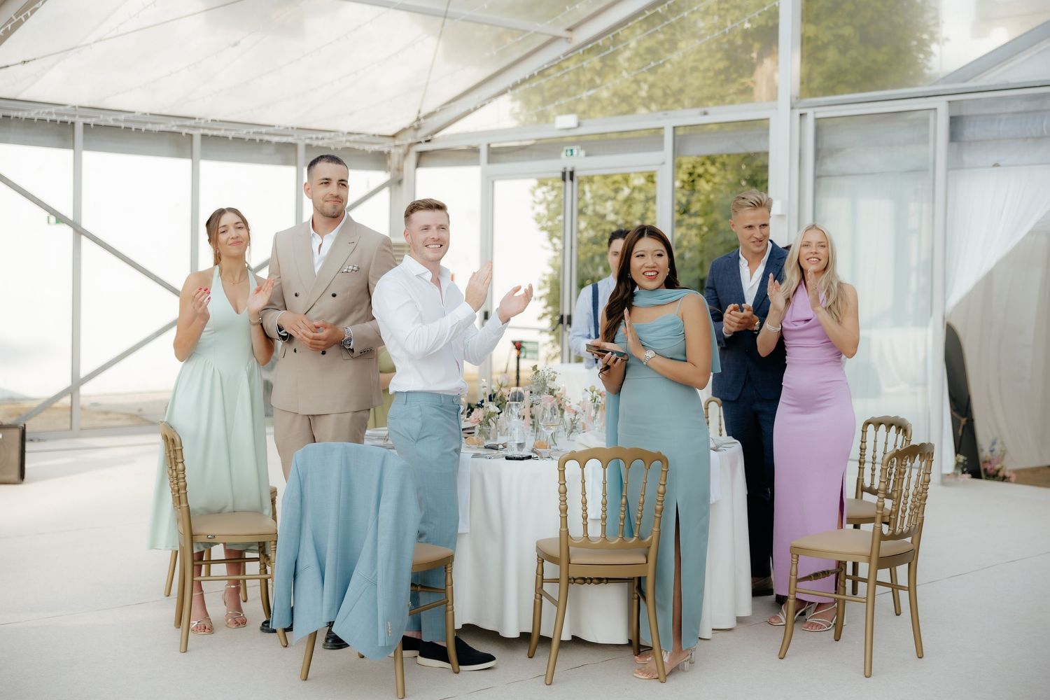 Wedding party members in pastel blue and lavender dresses pose together during a celebration event.