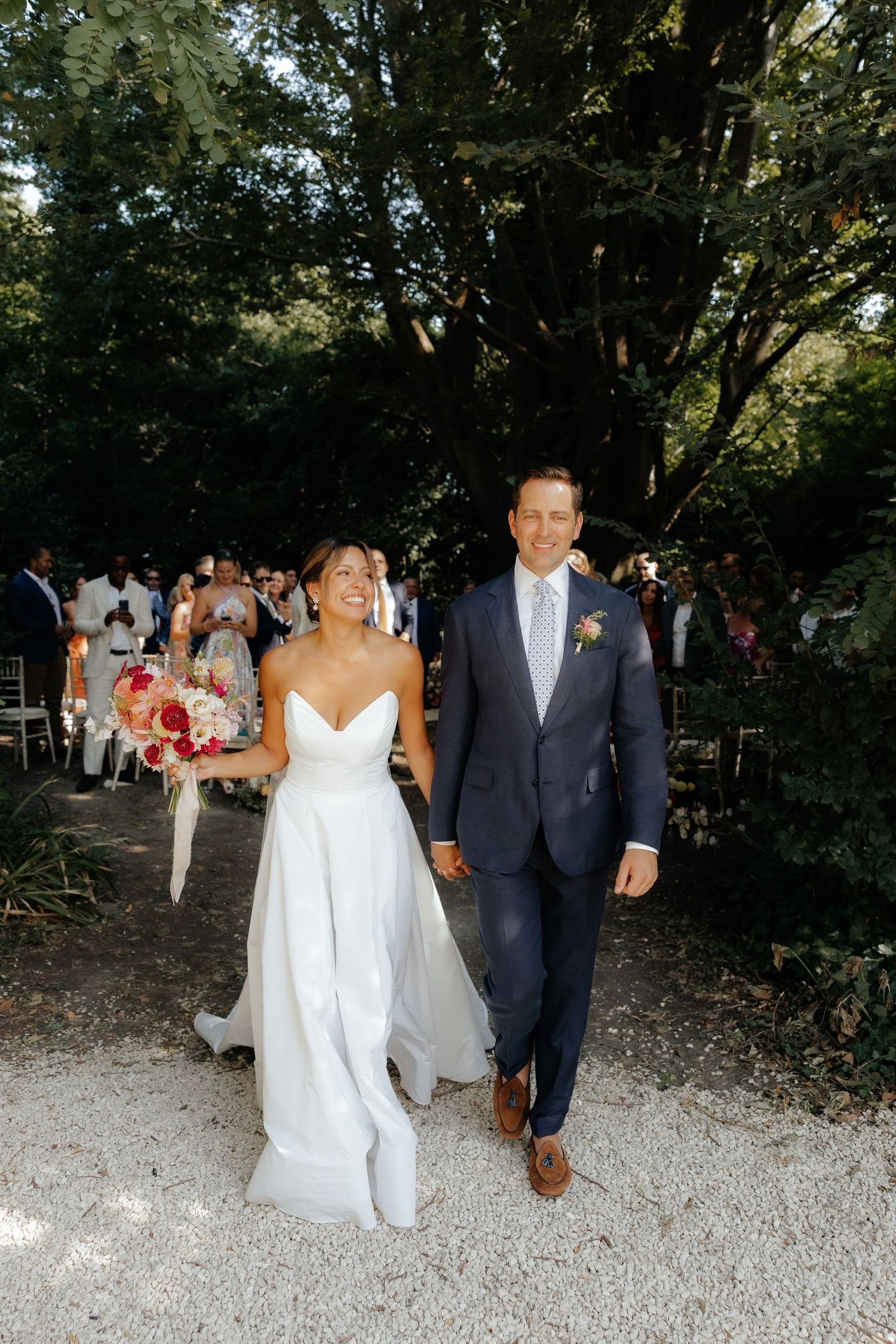 Wedding party walking along a gravel path surrounded by lush greenery.