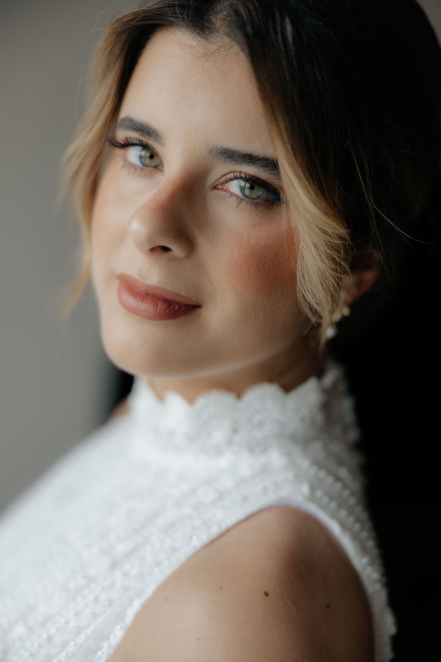 Close-up portrait of a bride with green eyes in a white scalloped lace high-neck wedding dress.